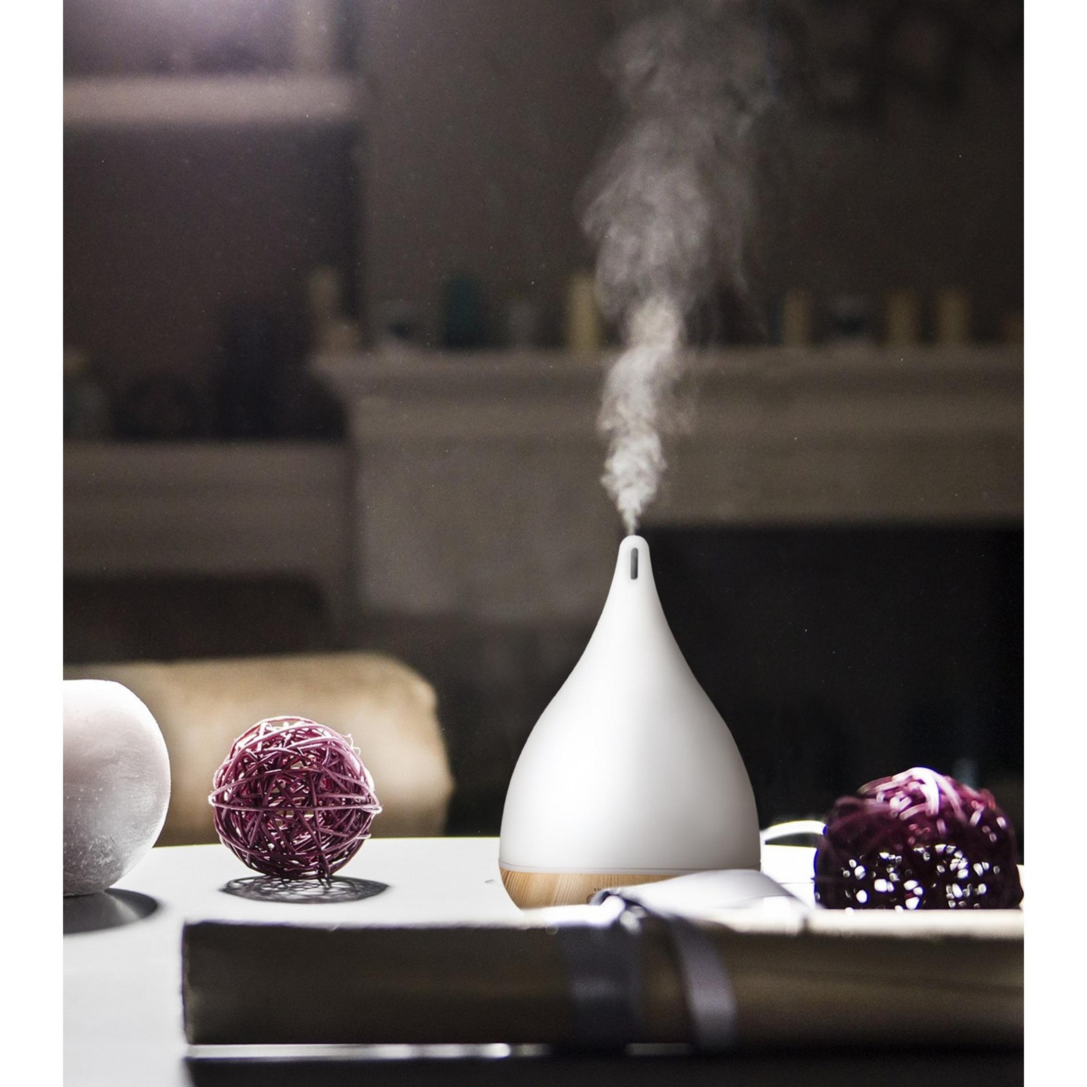 Un diffusore bianco rilascia vapore, con due palline decorative nelle vicinanze.