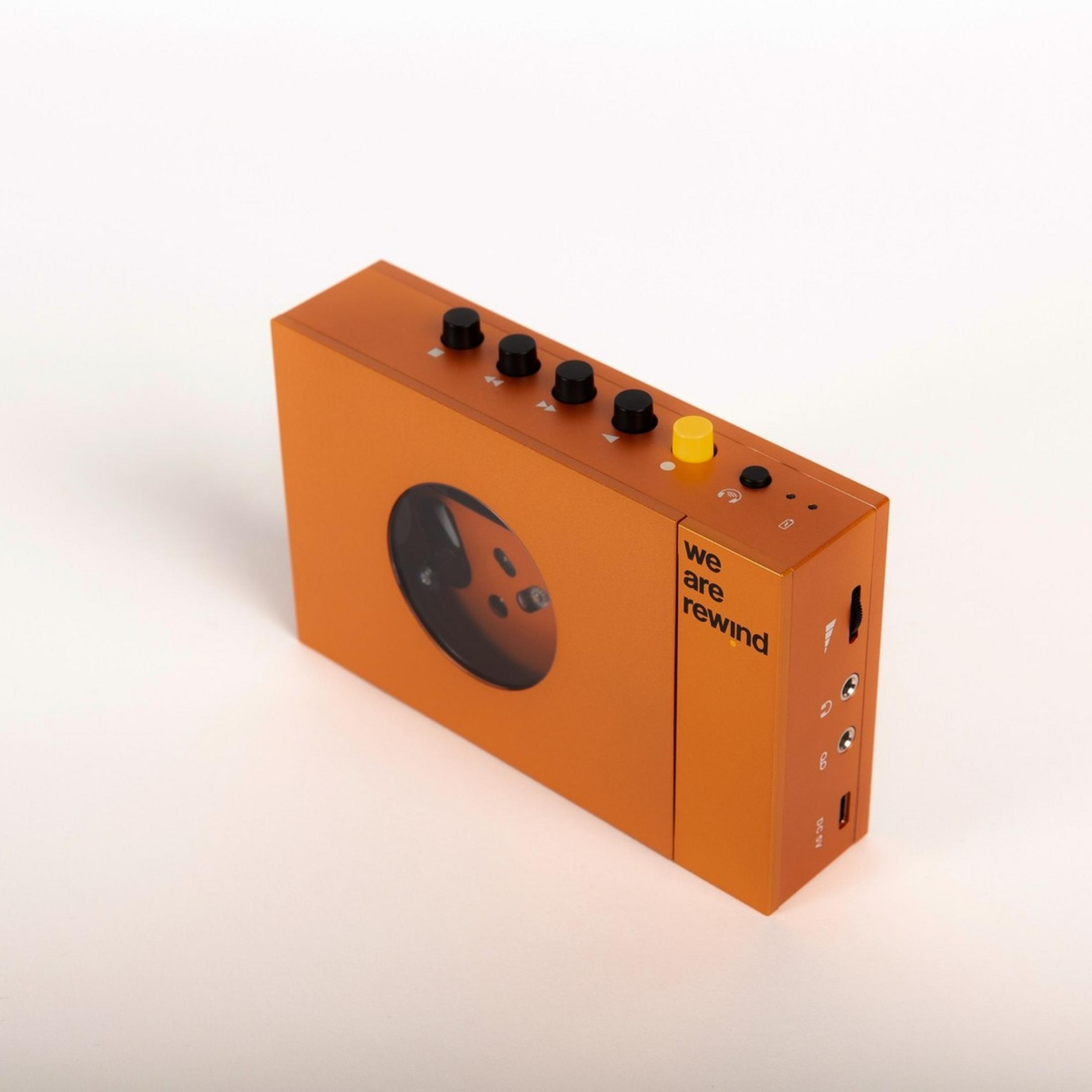 Lecteur de cassettes orange avec boutons noirs et une fenêtre montrant les bobines.