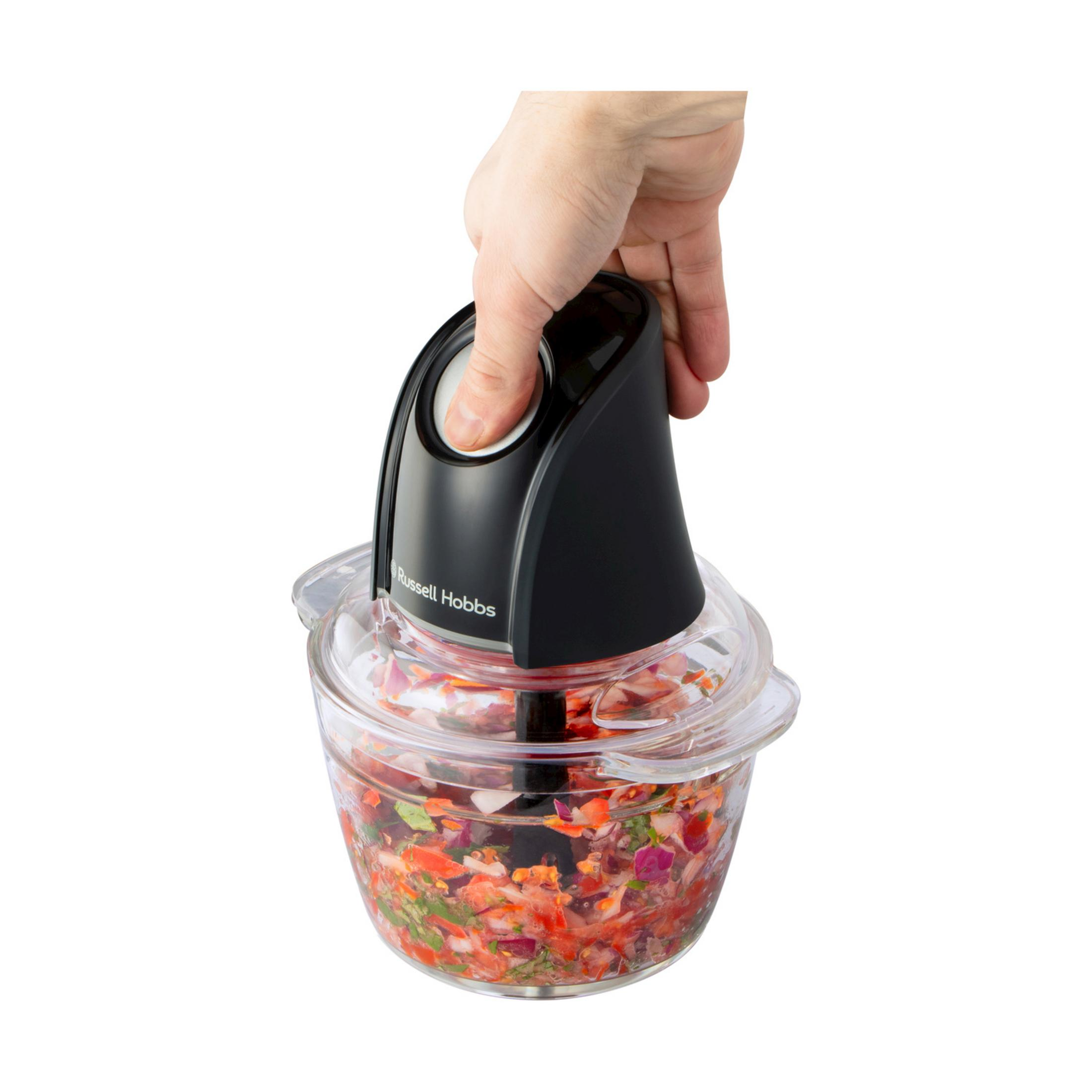Eine Hand drückt den Knopf eines Russell Hobbs Zerkleinerers mit gehacktem Gemüse.