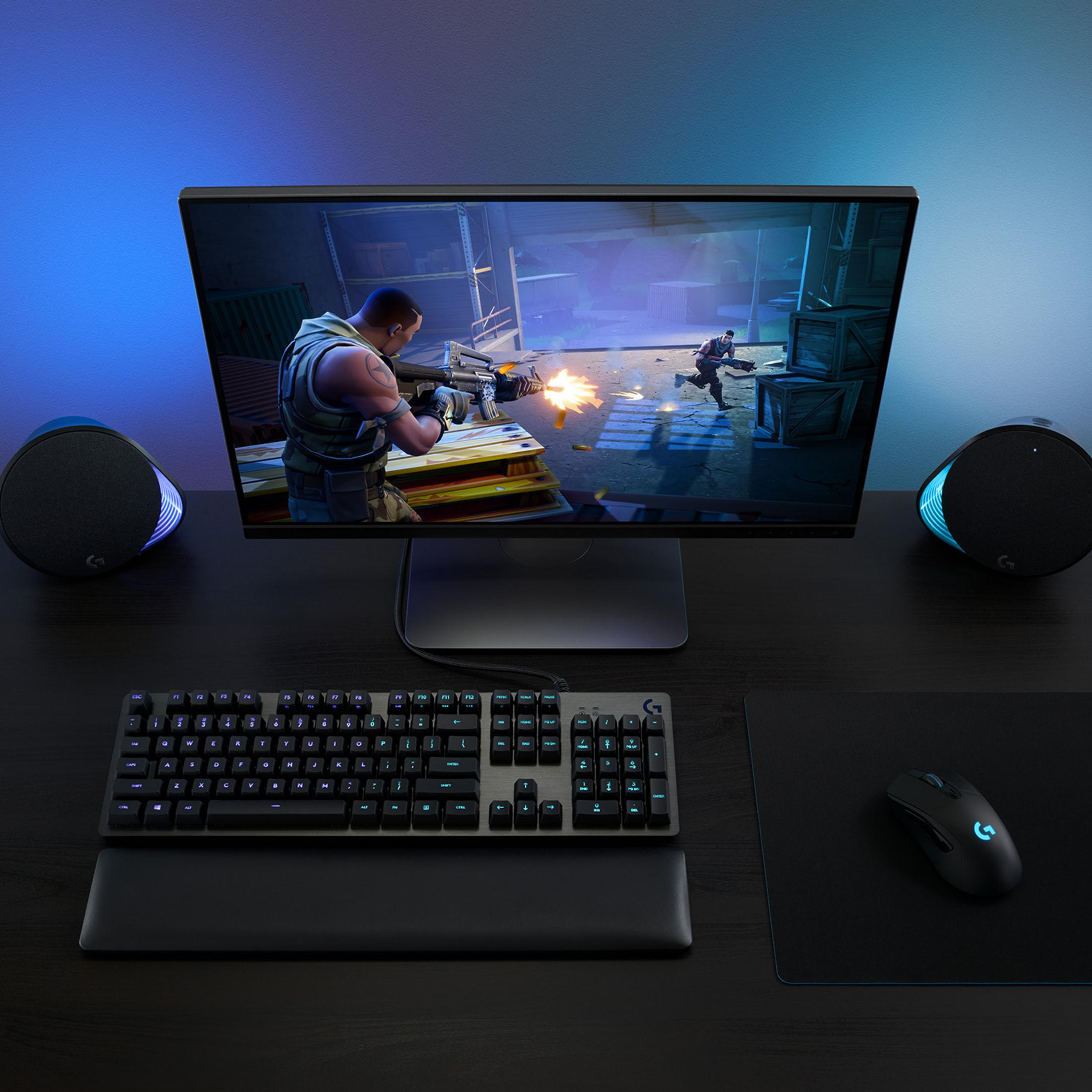Bureau met gaming-setup, monitor toont een spel, toetsenbord, muis, luidsprekers.