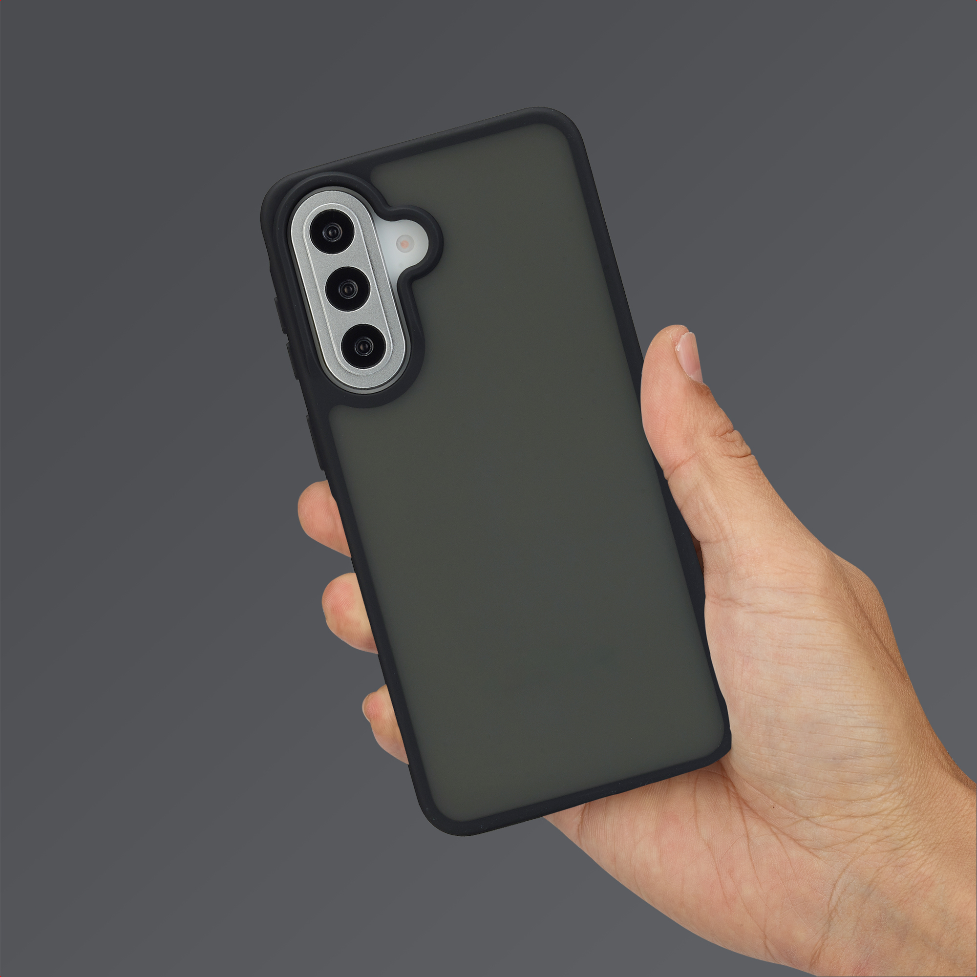 Une main tient un téléphone gris foncé à triple caméra sur fond gris.