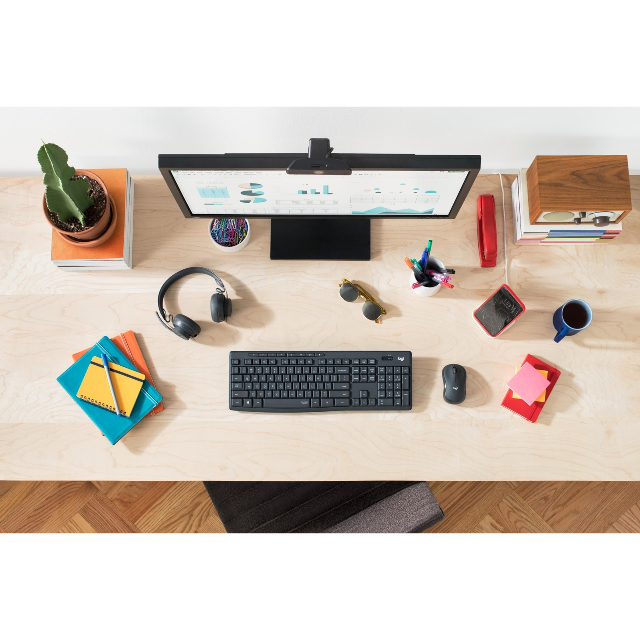 Biurko z monitorem, klawiaturą, myszą, słuchawkami, notatnikami i rośliną.