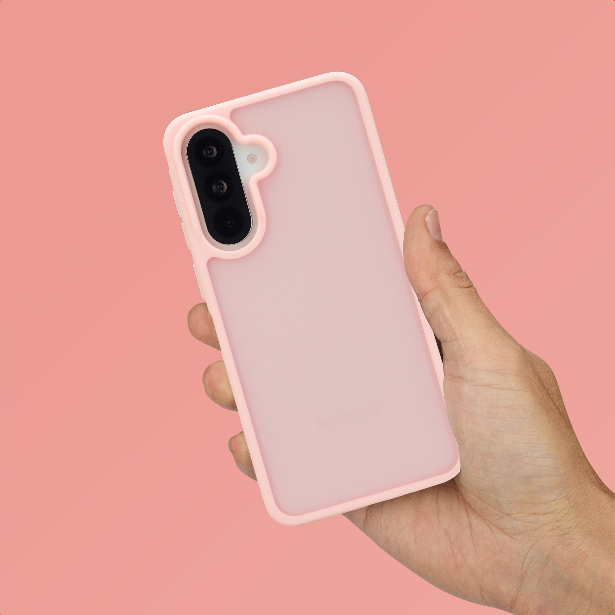 Een hand houdt een lichtroze telefoon met drievoudige camera vast op roze achtergrond.