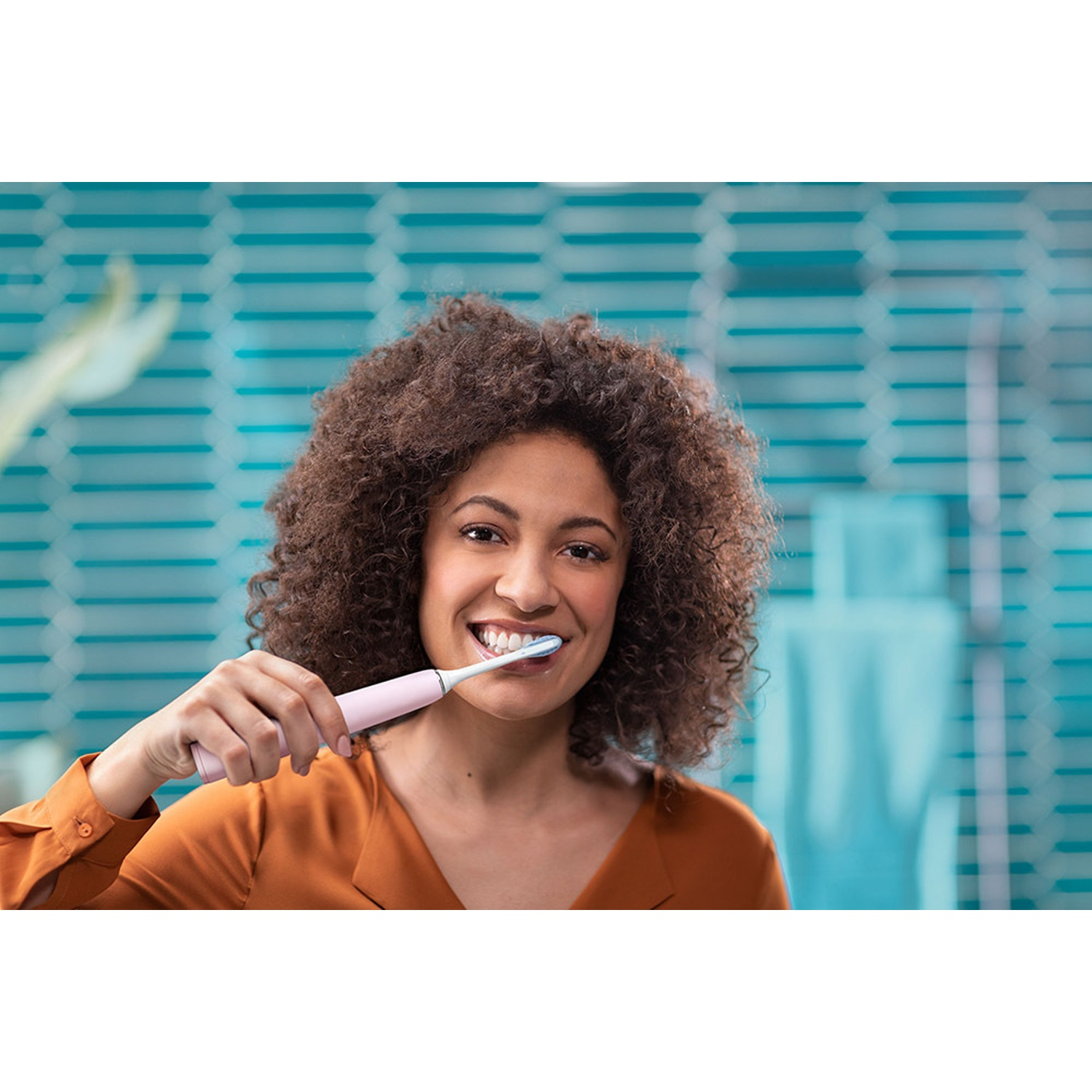 Una mujer con pelo rizado se cepilla los dientes con un cepillo eléctrico rosa.