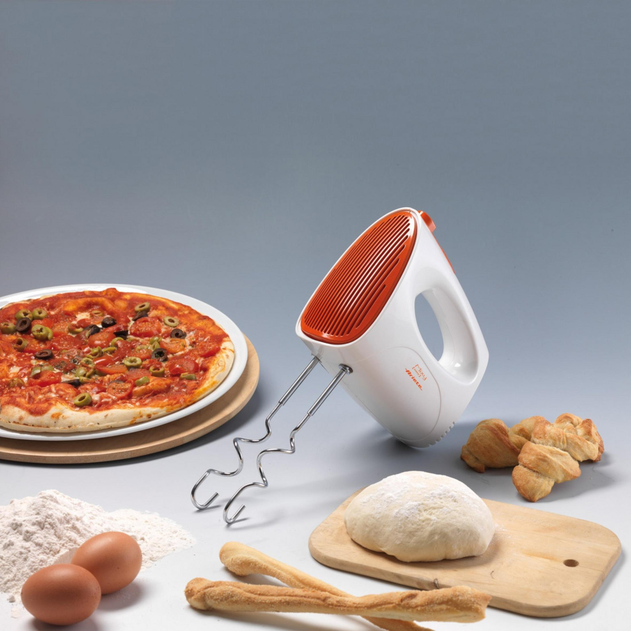 Ein Handmixer mit orangefarbenem Akzent neben einer Pizza, Teig, Eiern und Gebäck.