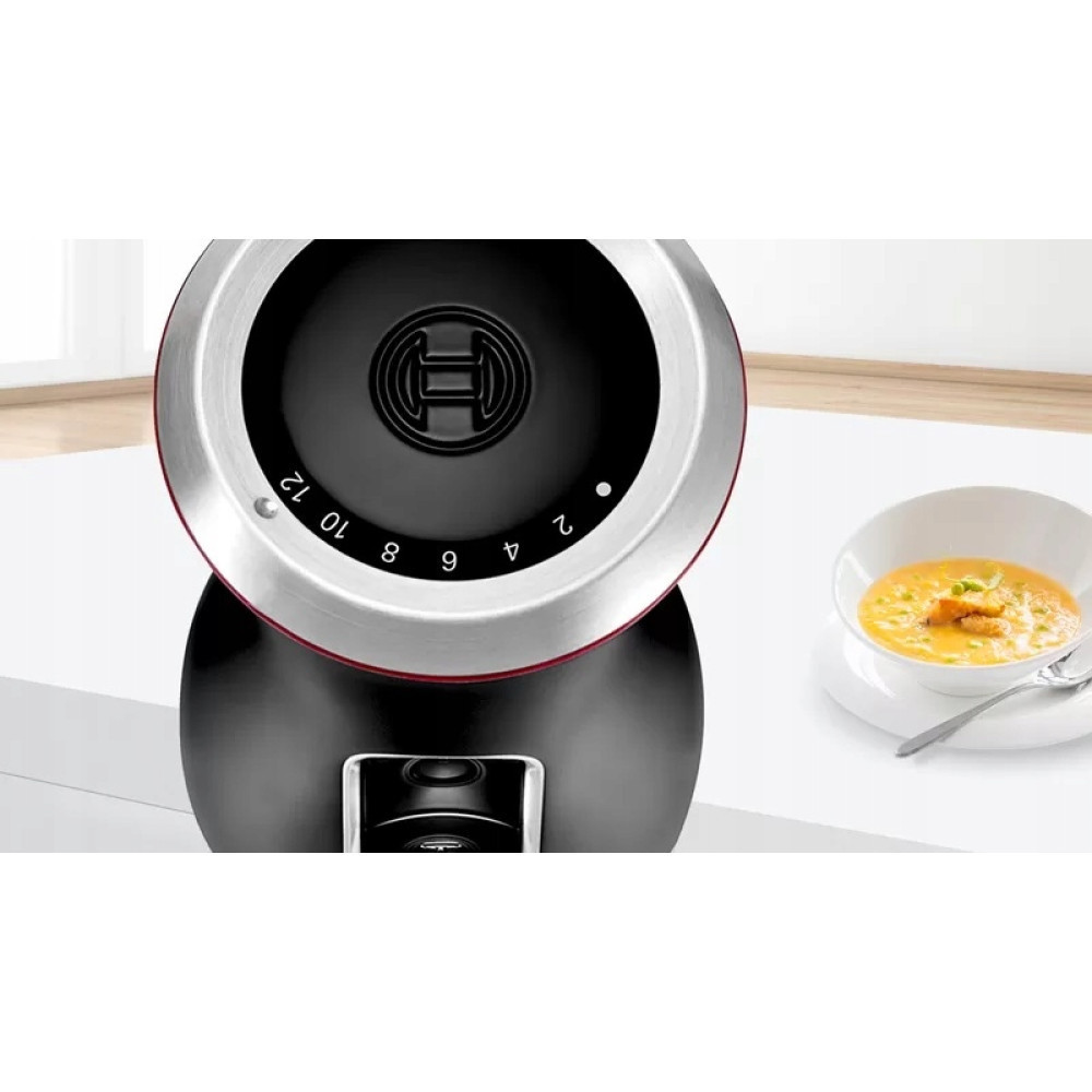 Ein schwarzer Mixer mit silbernem Ring und einer Schüssel Suppe daneben.