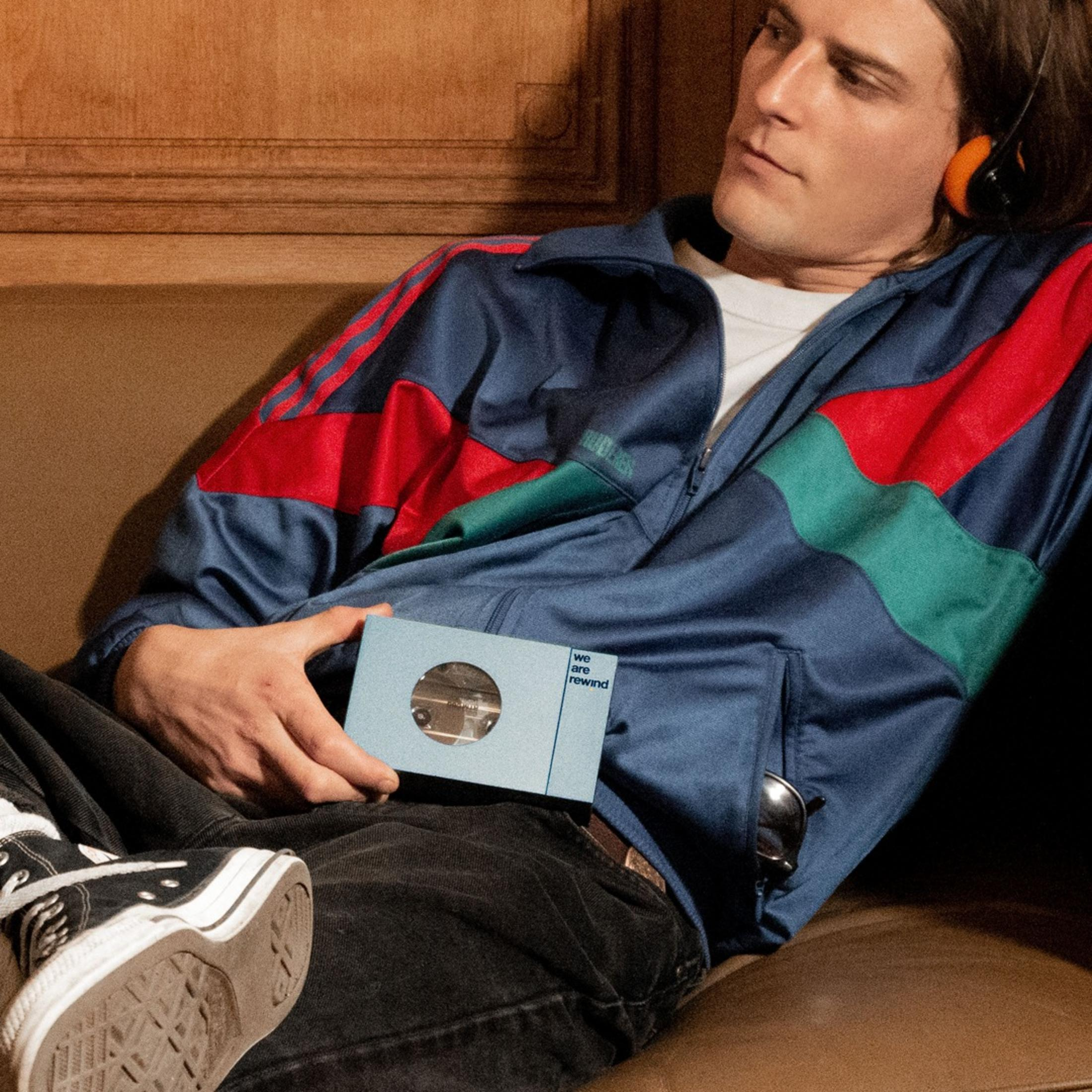 Un homme avec des écouteurs et une veste rétro tient une cassette.