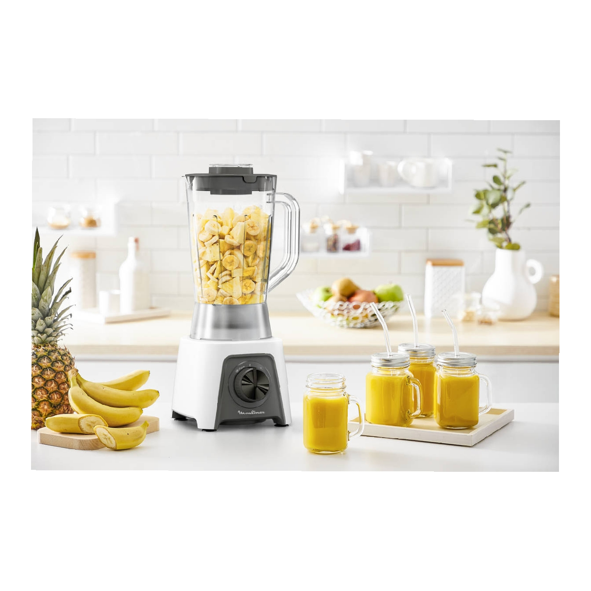 Un frullatore con banane, un ananas e tre bicchieri di succo su un bancone da cucina.