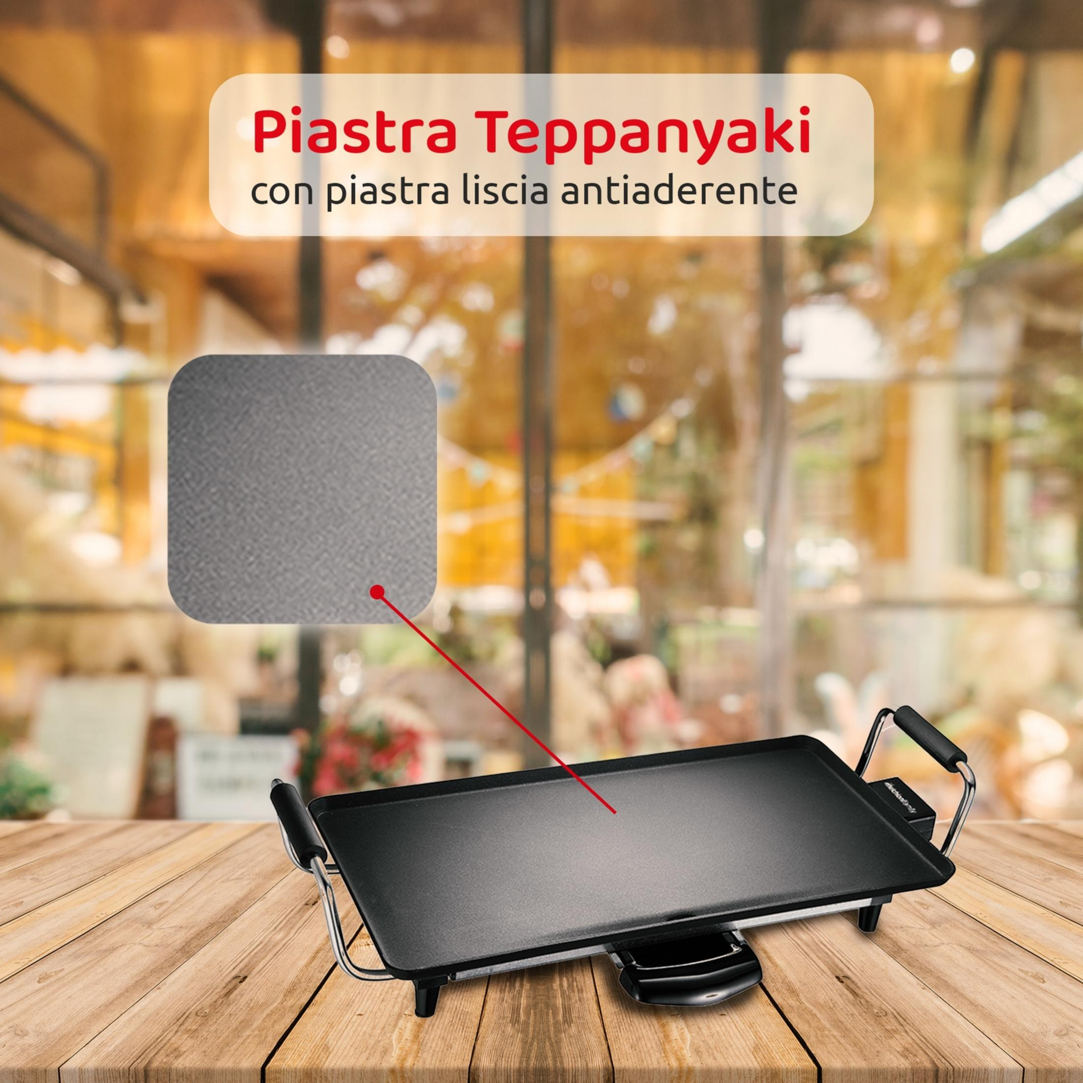 Eine schwarze Teppanyaki-Grillplatte mit Griffen auf einem Holztisch.