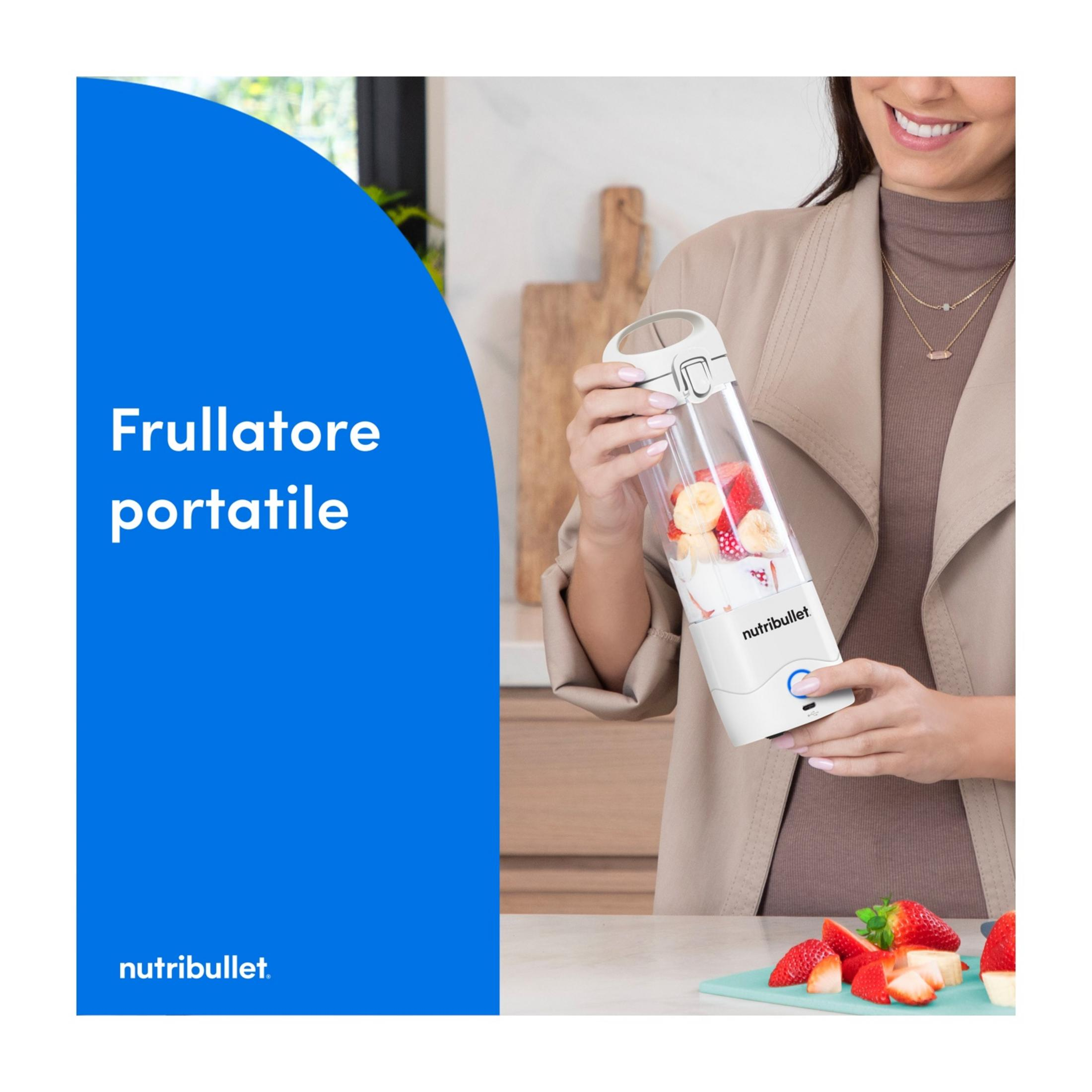 Eine Frau hält einen Mixer mit Früchten. Erdbeeren und Bananen liegen daneben.