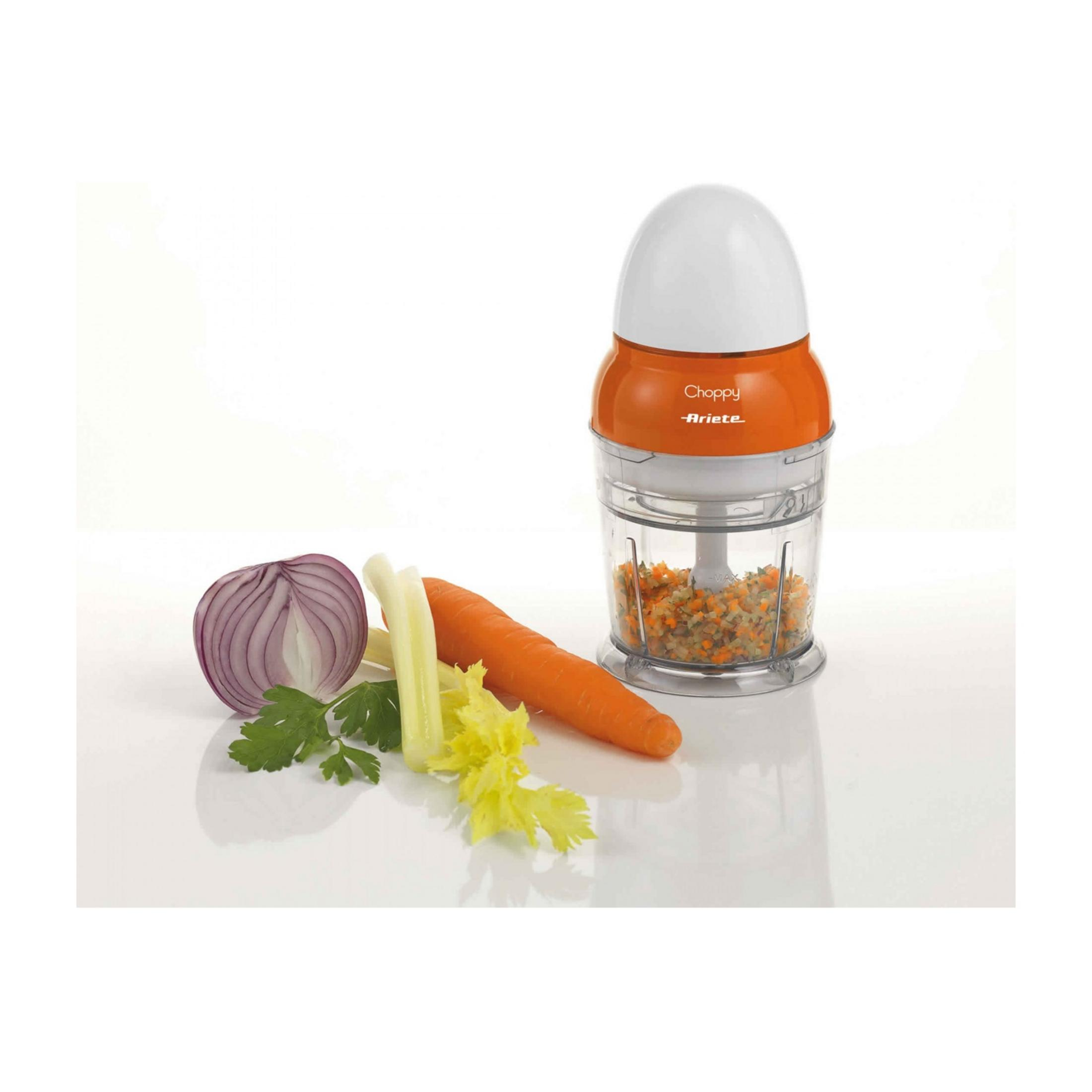 Ein orangefarbener Küchenhäcksler mit gehacktem Gemüse und frischem Gemüse daneben.