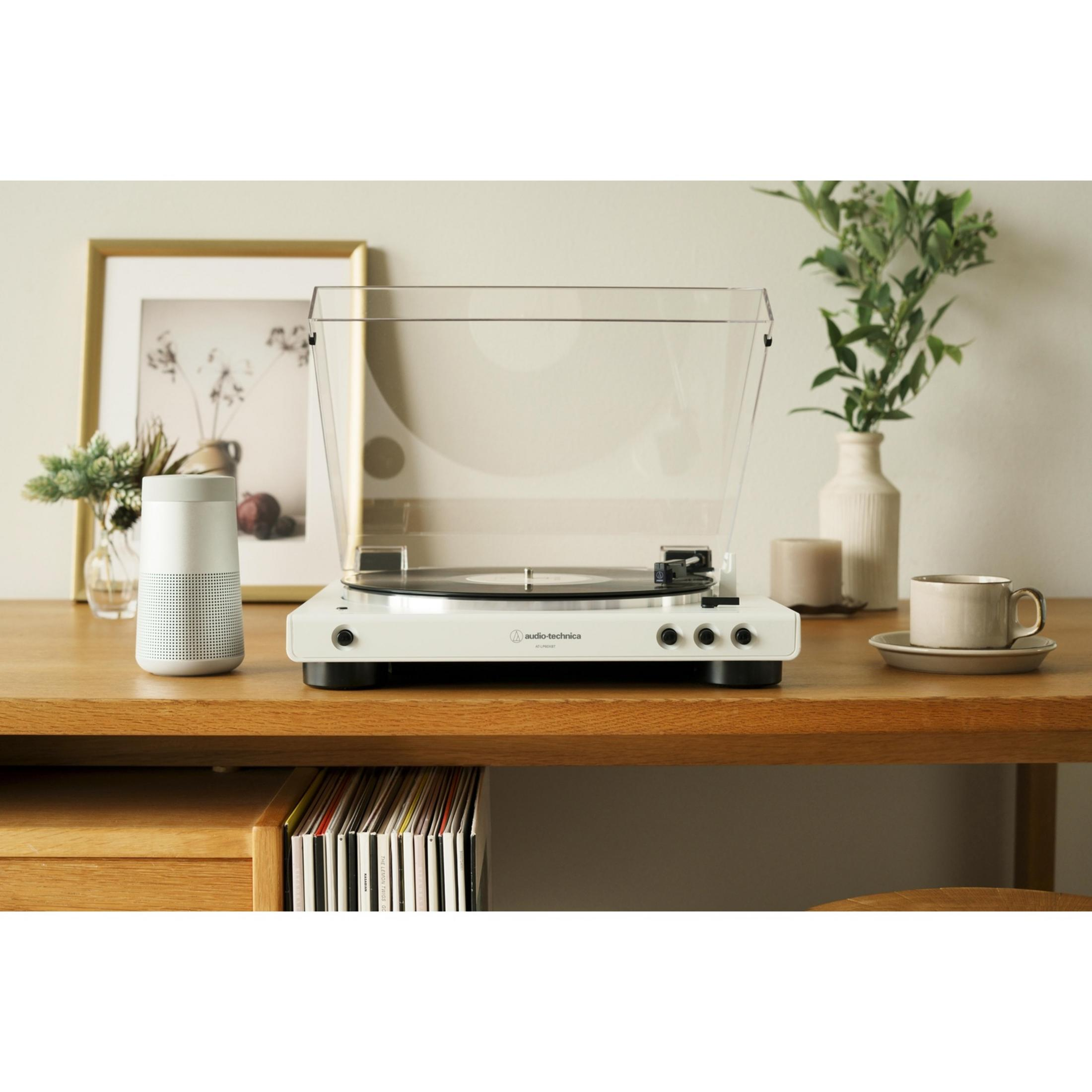 Un giradischi bianco con un disco in vinile, accanto un altoparlante e una cornice.