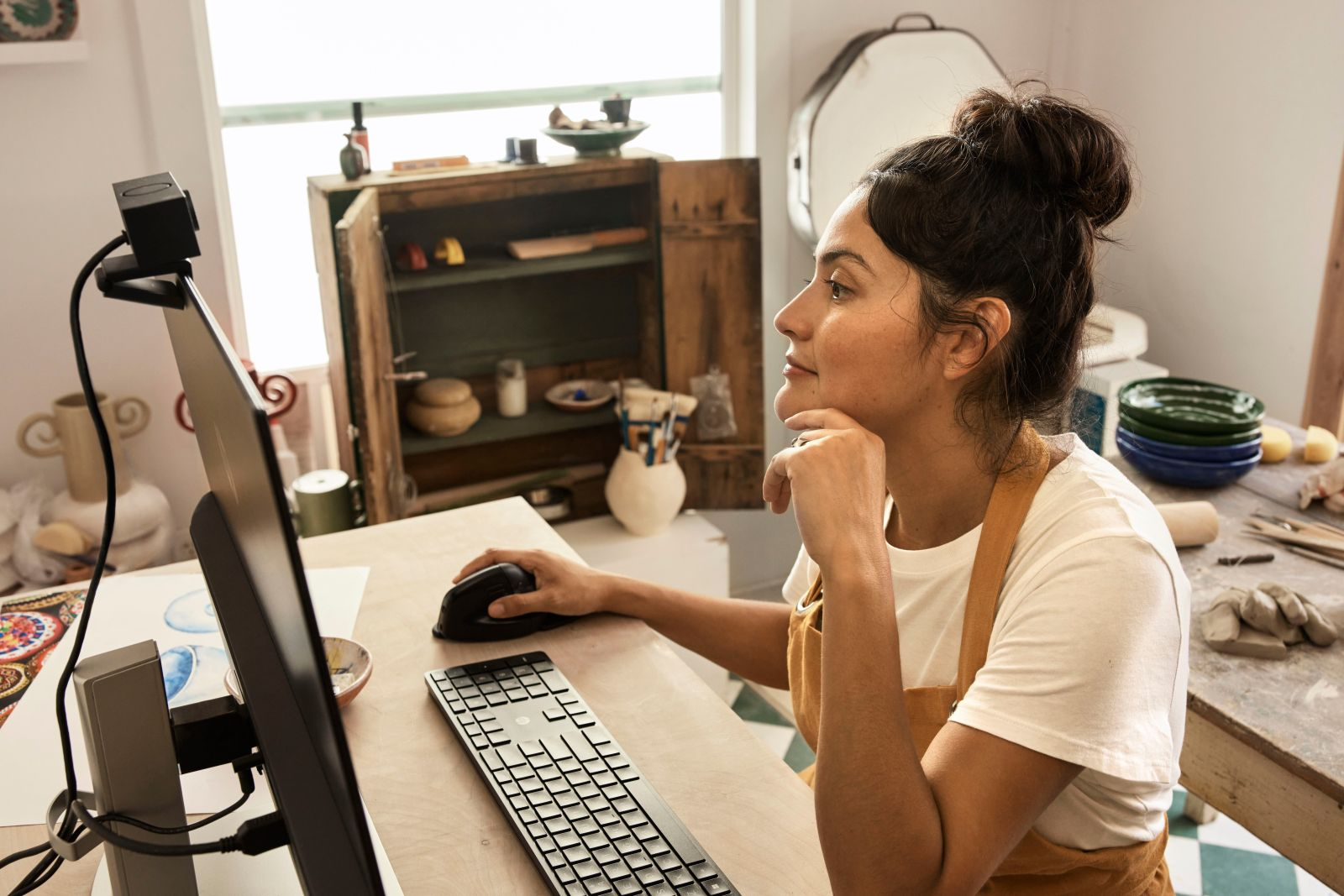 Kobieta siedzi przy biurku z komputerem i kamerą internetową.