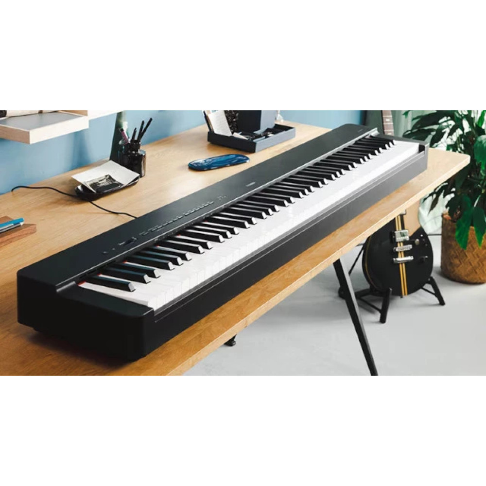 Czarny pianino cyfrowe stoi na drewnianym stole. Po prawej stronie gitara.