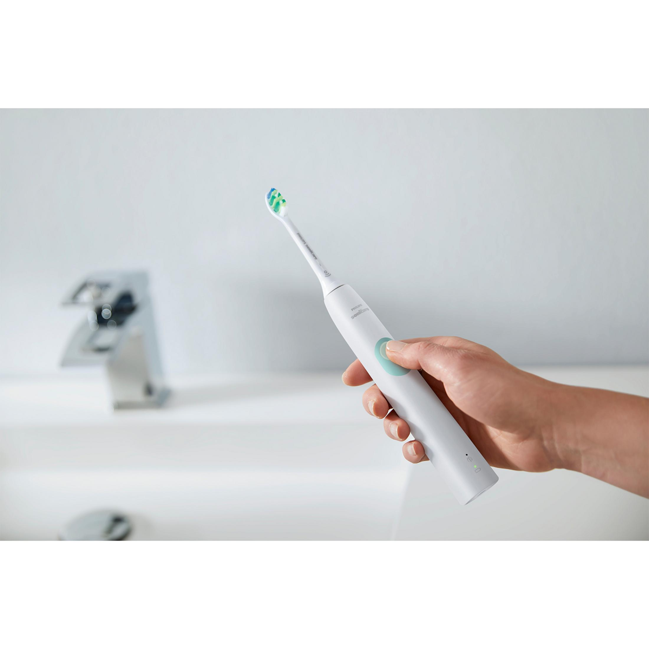Una mano tiene uno spazzolino elettrico bianco con testina blu-verde sopra un lavandino.