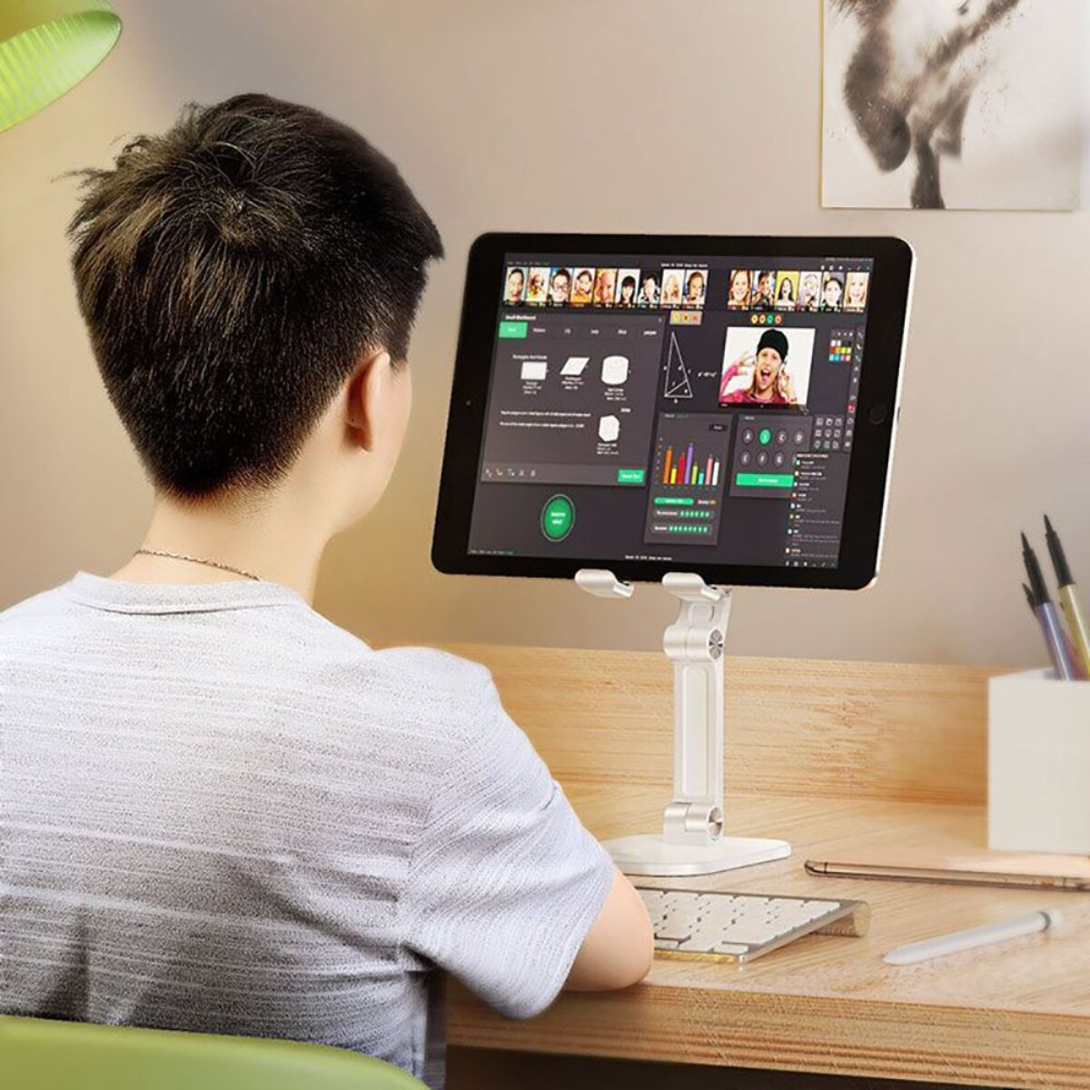 Eine Person sitzt am Schreibtisch und schaut auf ein Tablet mit einer Videokonferenz.