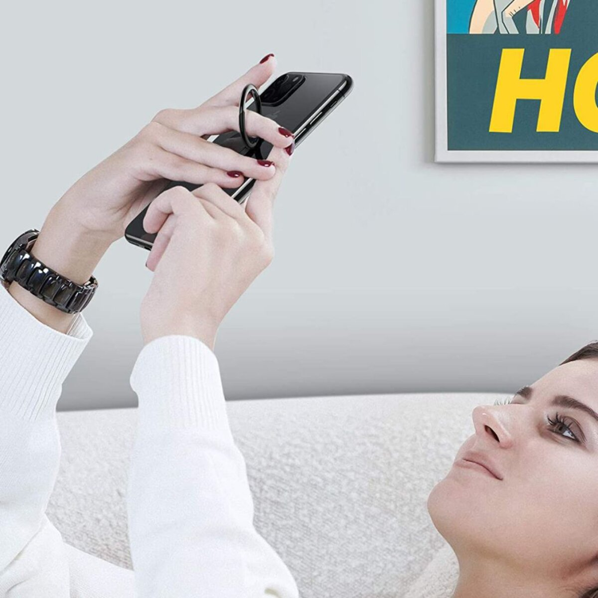 Eine Frau liegt auf einer Couch und hält ein Smartphone mit einem Ringhalter.