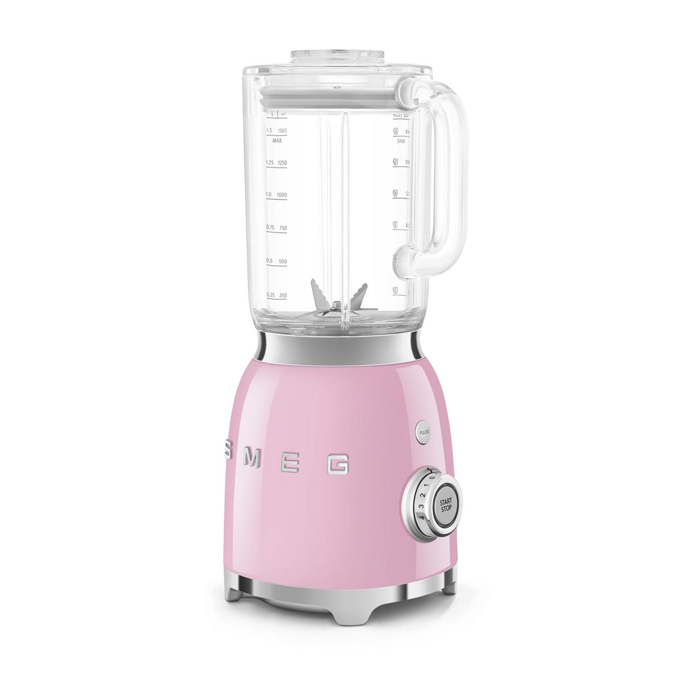 Cam sürahili ve gümüş aksanlı pembe Smeg blender beyaz zeminde duruyor.