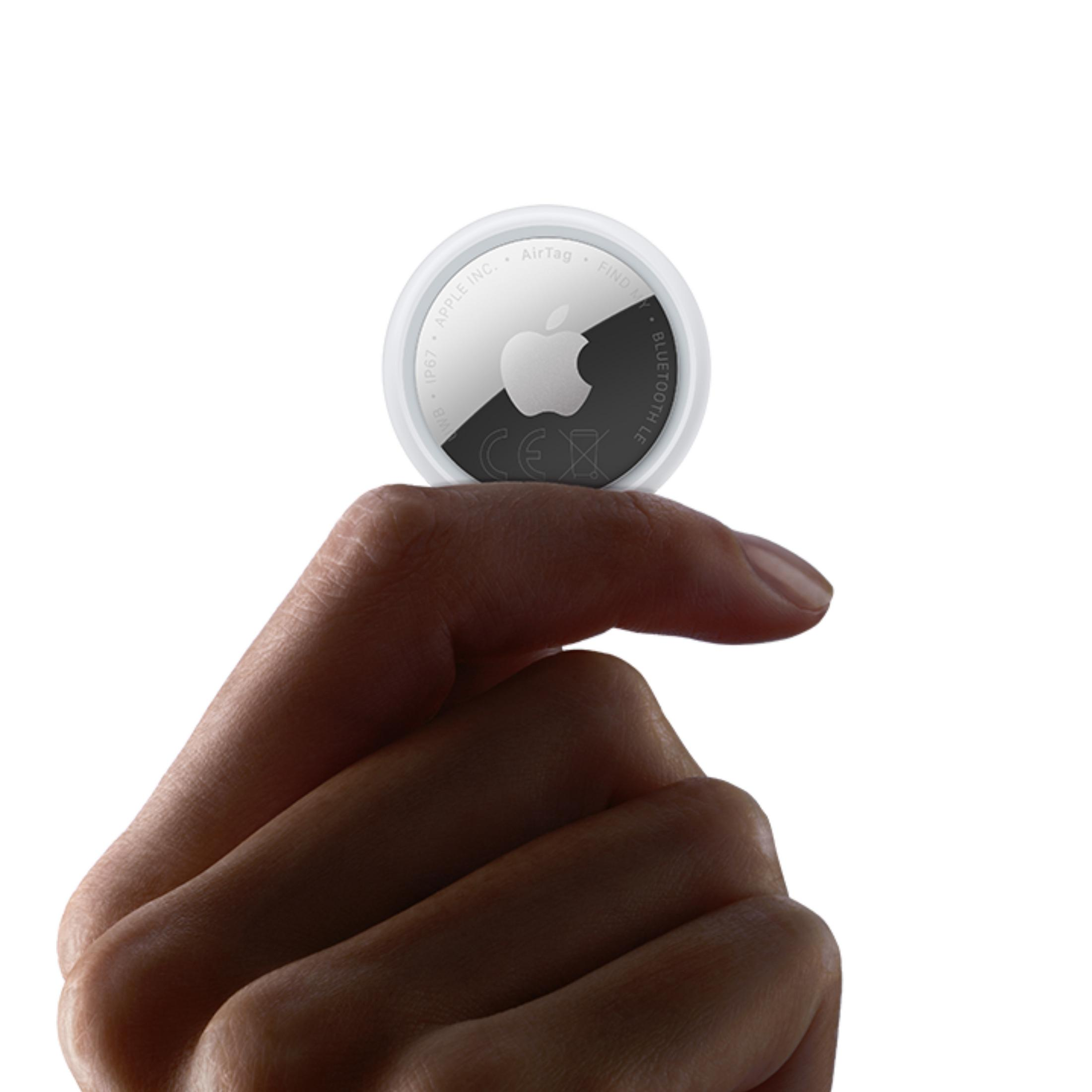 Una mano tiene un Apple AirTag bianco e rotondo con logo di mela.