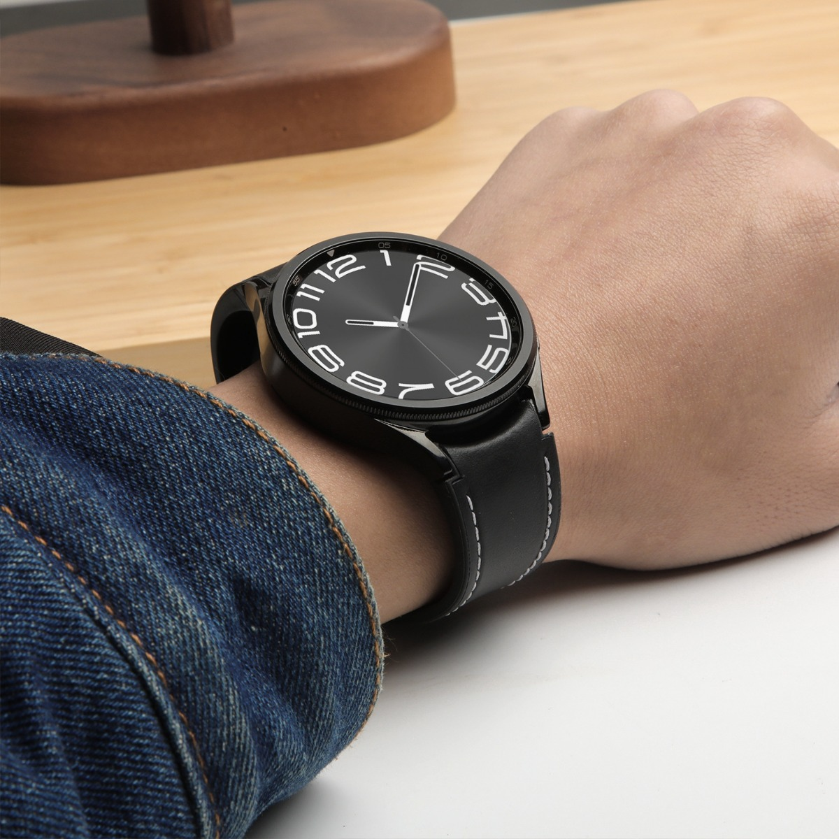 Una persona indossa uno smartwatch nero con quadrante bianco e cinturino in pelle nera.