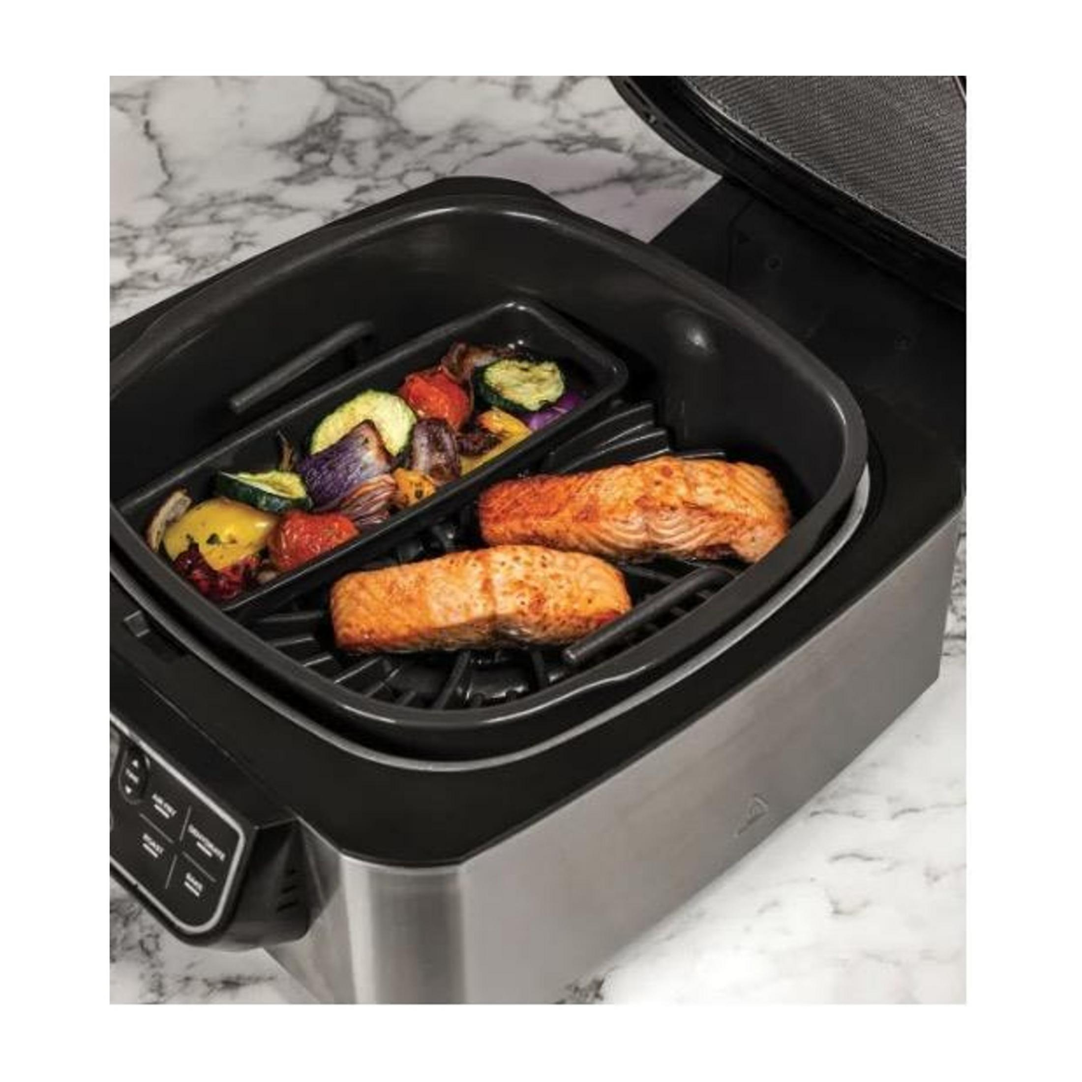 Zwei Lachsfilets und gegrilltes Gemüse in einem schwarzen Airfryer auf Marmorunterlage.