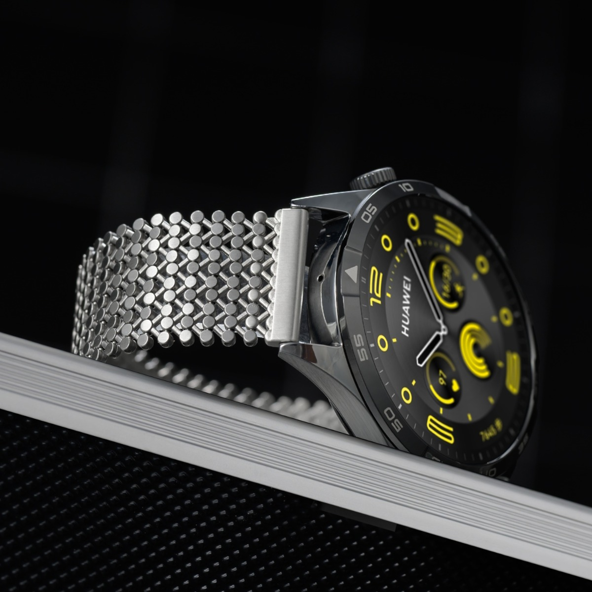 Uno smartwatch argentato con quadrante nero e accenti gialli.