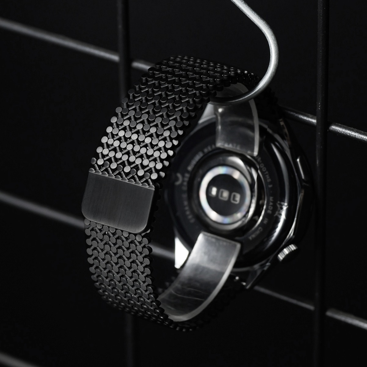 Schwarzes Mesh-Armband an einer Smartwatch, die an einem Haken hängt.
