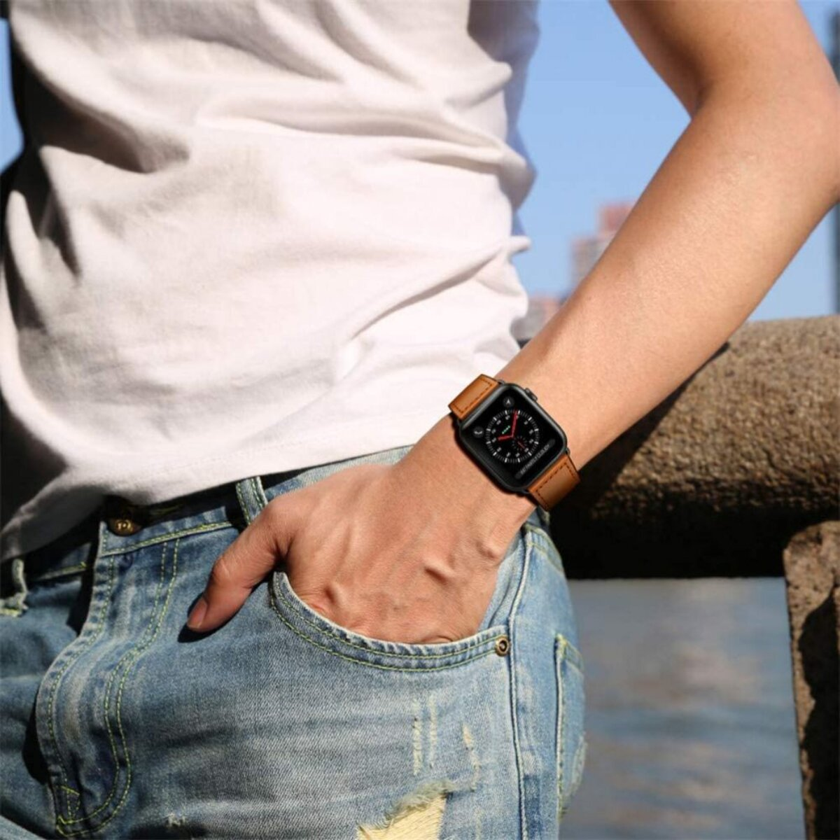Eine Person mit Jeans und weißem T-Shirt trägt eine Smartwatch mit braunem Armband.