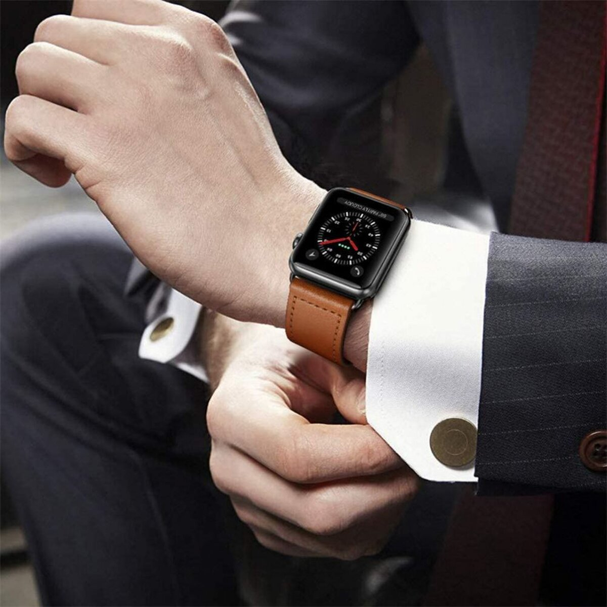 Ein Mann im Anzug trägt eine schwarze Smartwatch mit braunem Lederarmband am linken Handgelenk.