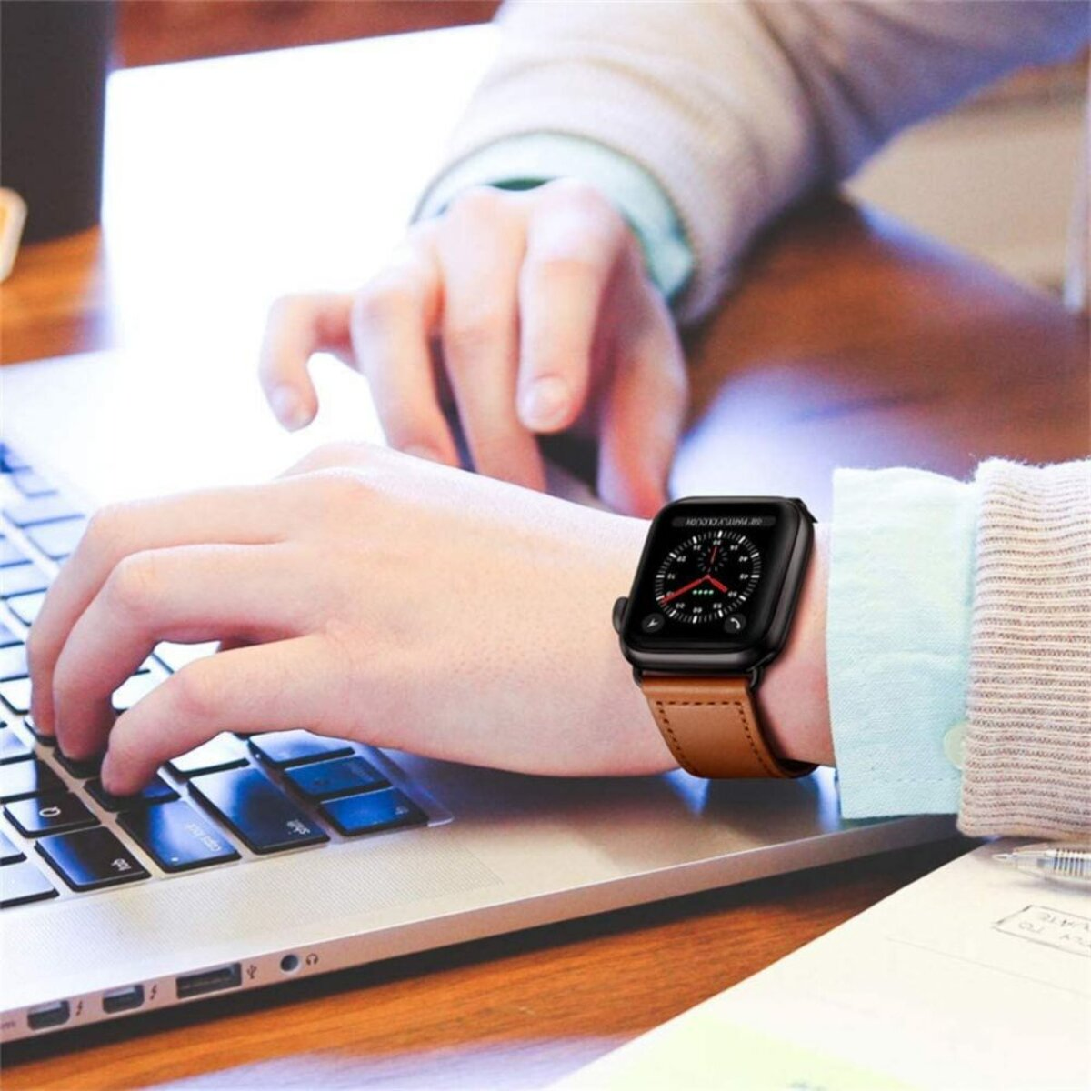 Eine Person tippt auf einer Tastatur, trägt eine Smartwatch mit braunem Lederarmband.