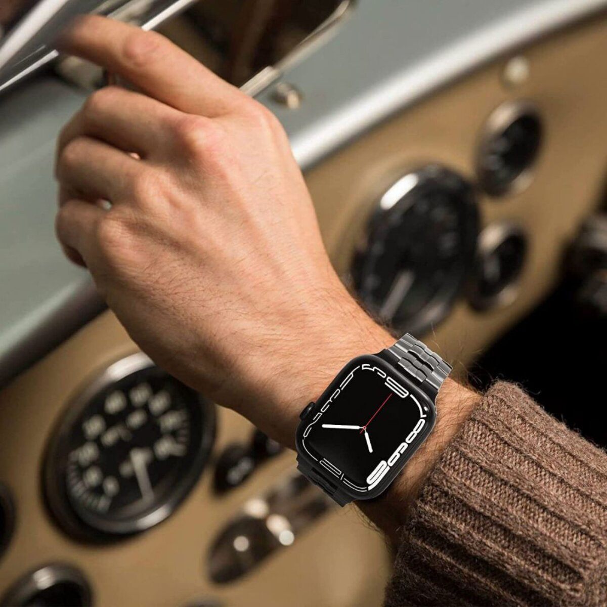Mann in einem braunen Pullover mit einer Smartwatch am Handgelenk, der im Auto sitzt.