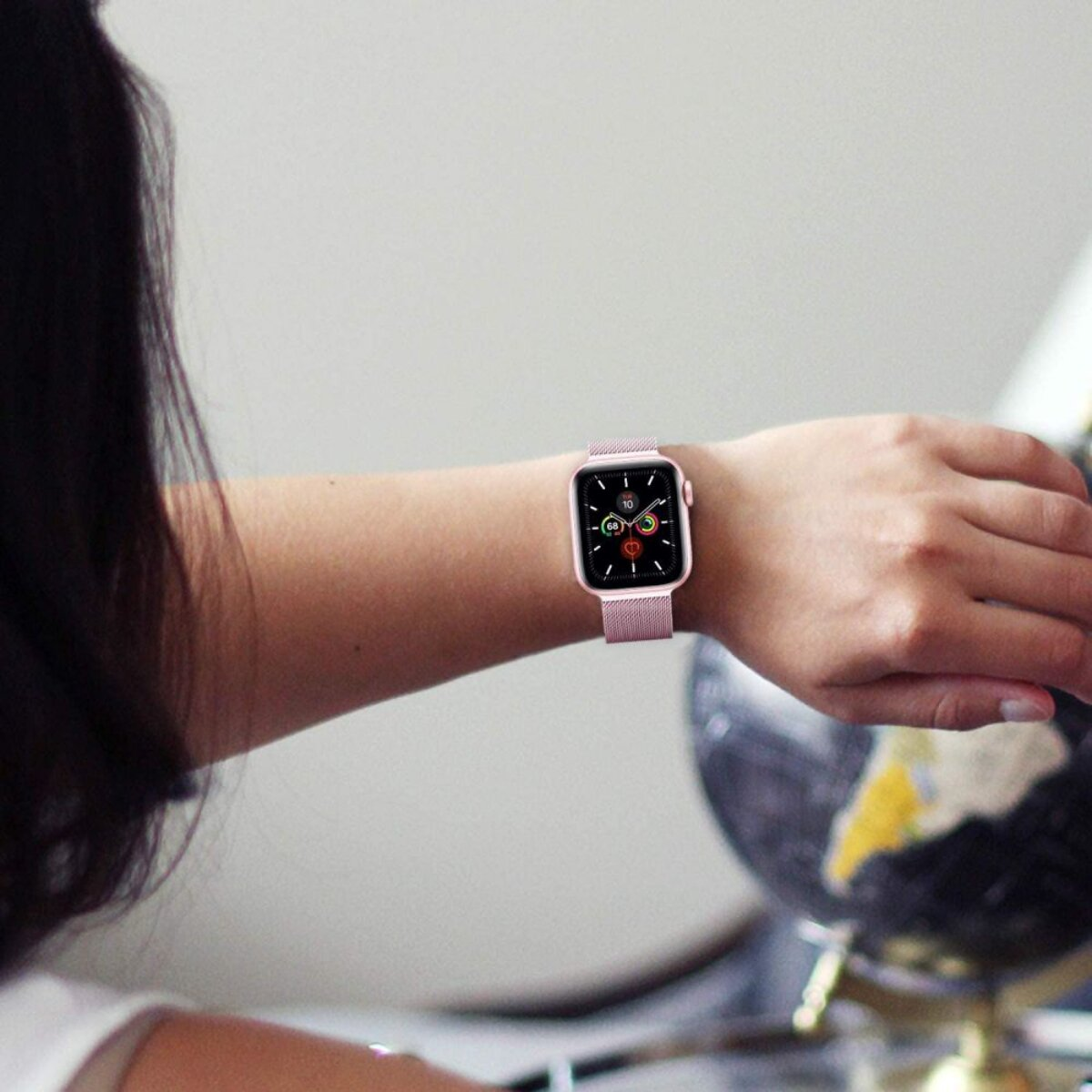 Eine Frau mit einer roségoldenen Smartwatch am Handgelenk, die auf eine Weltkugel blickt.
