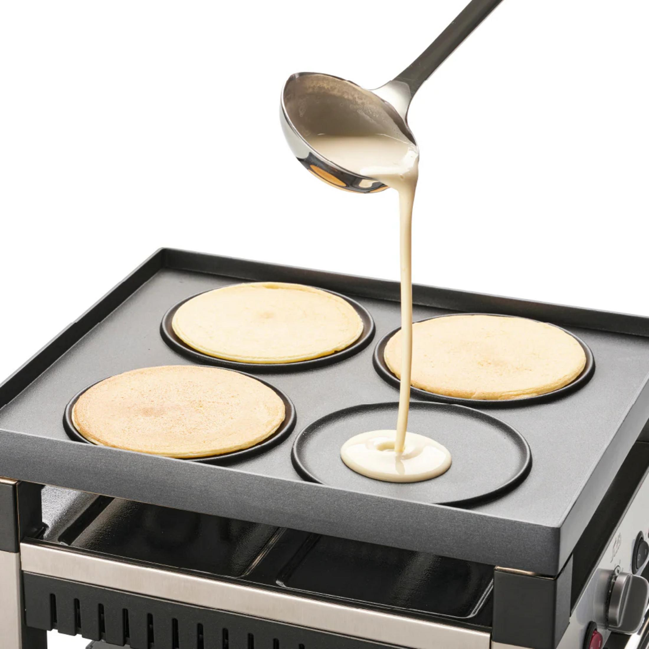 Eine Kelle mit Teig gießt Teig auf eine flache Grillplatte mit Pfannkuchen.
