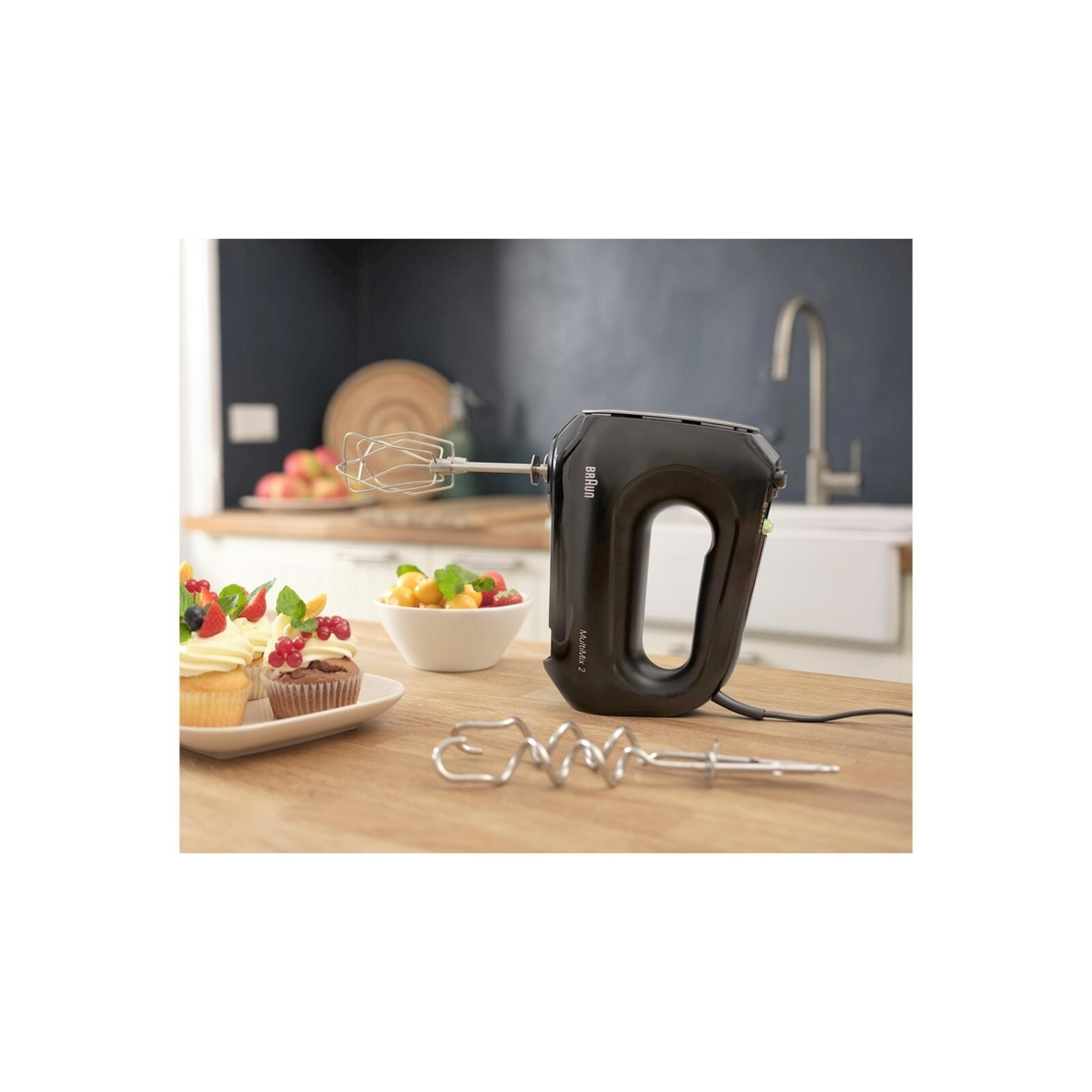 Schwarzer Braun Handmixer mit Rührbesen und verzierte Cupcakes auf Holzkountr.