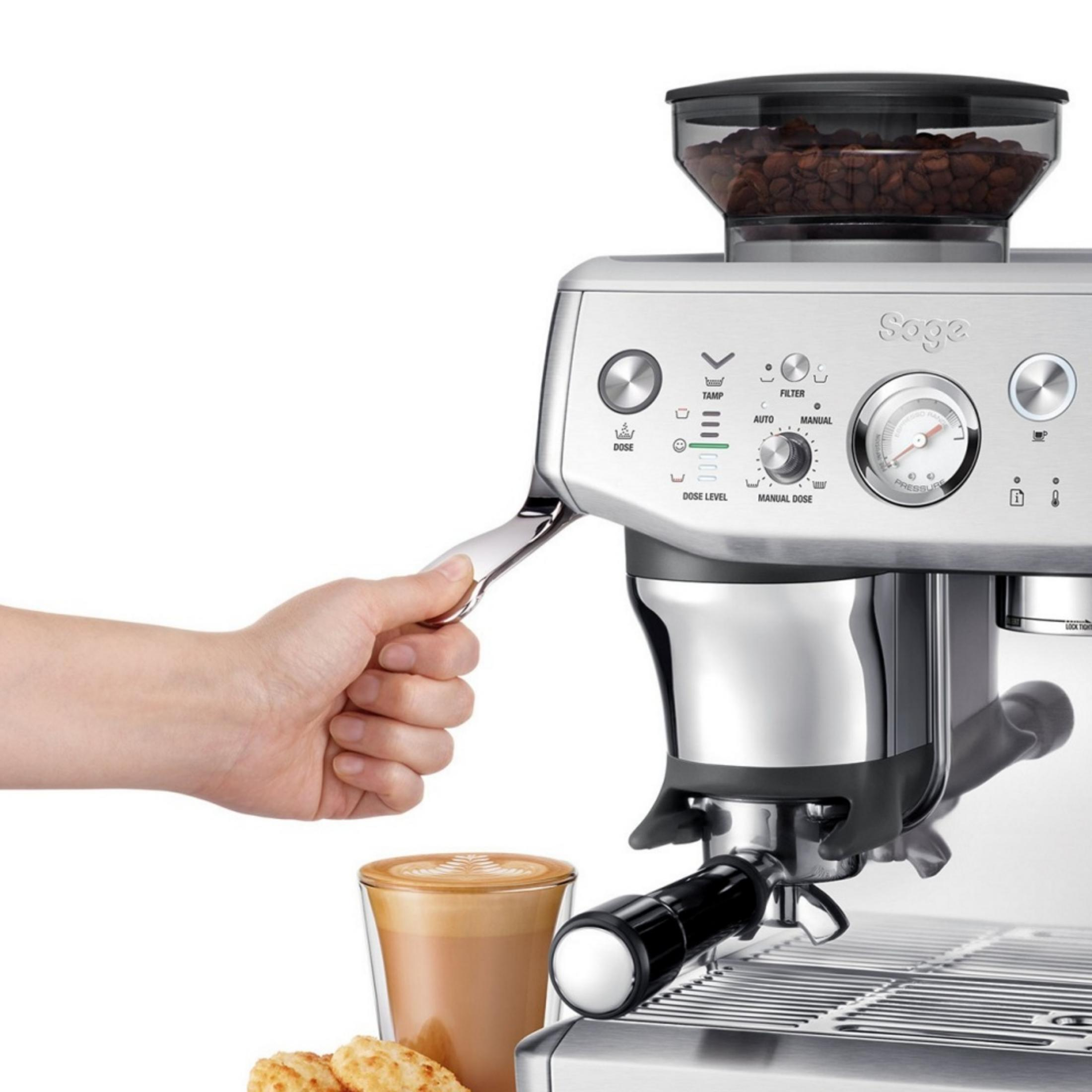 Une main actionne un levier sur une machine à café avec un réservoir à grains.
