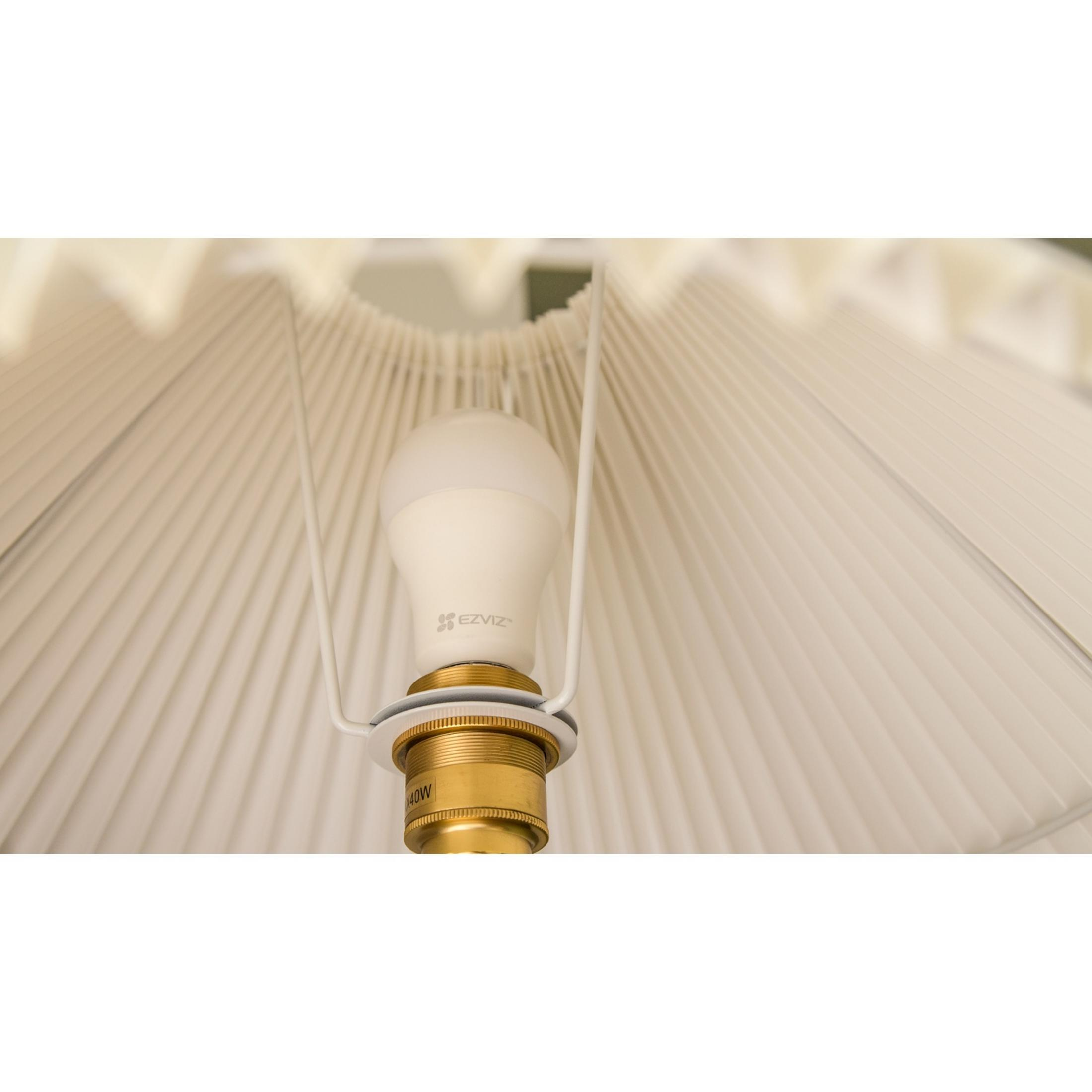 Una lampadina bianca EZVIZ in un portalampada d'ottone davanti a un paralume plissettato.