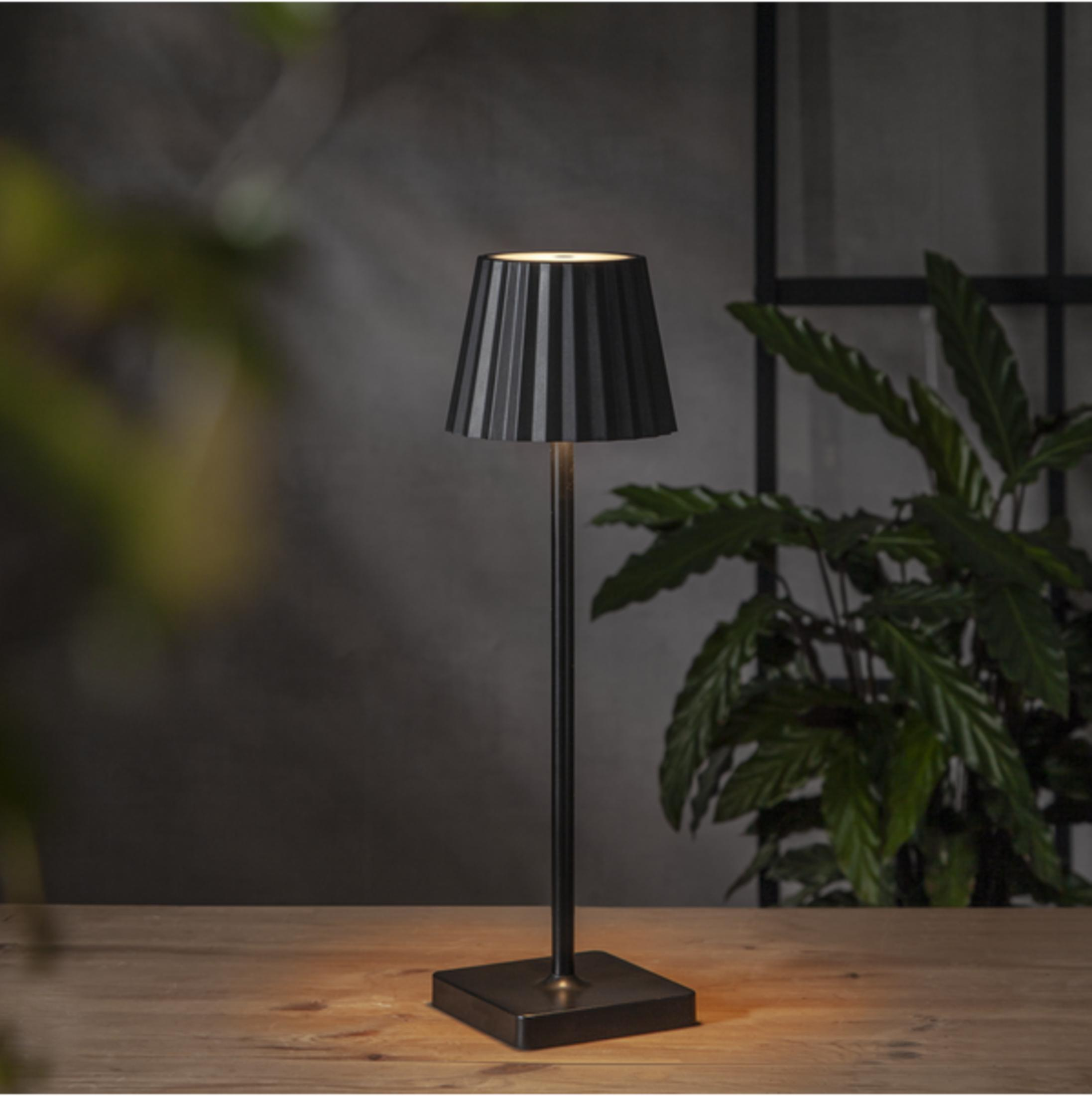 Una lampada da tavolo nera con paralume a coste su un tavolo di legno.