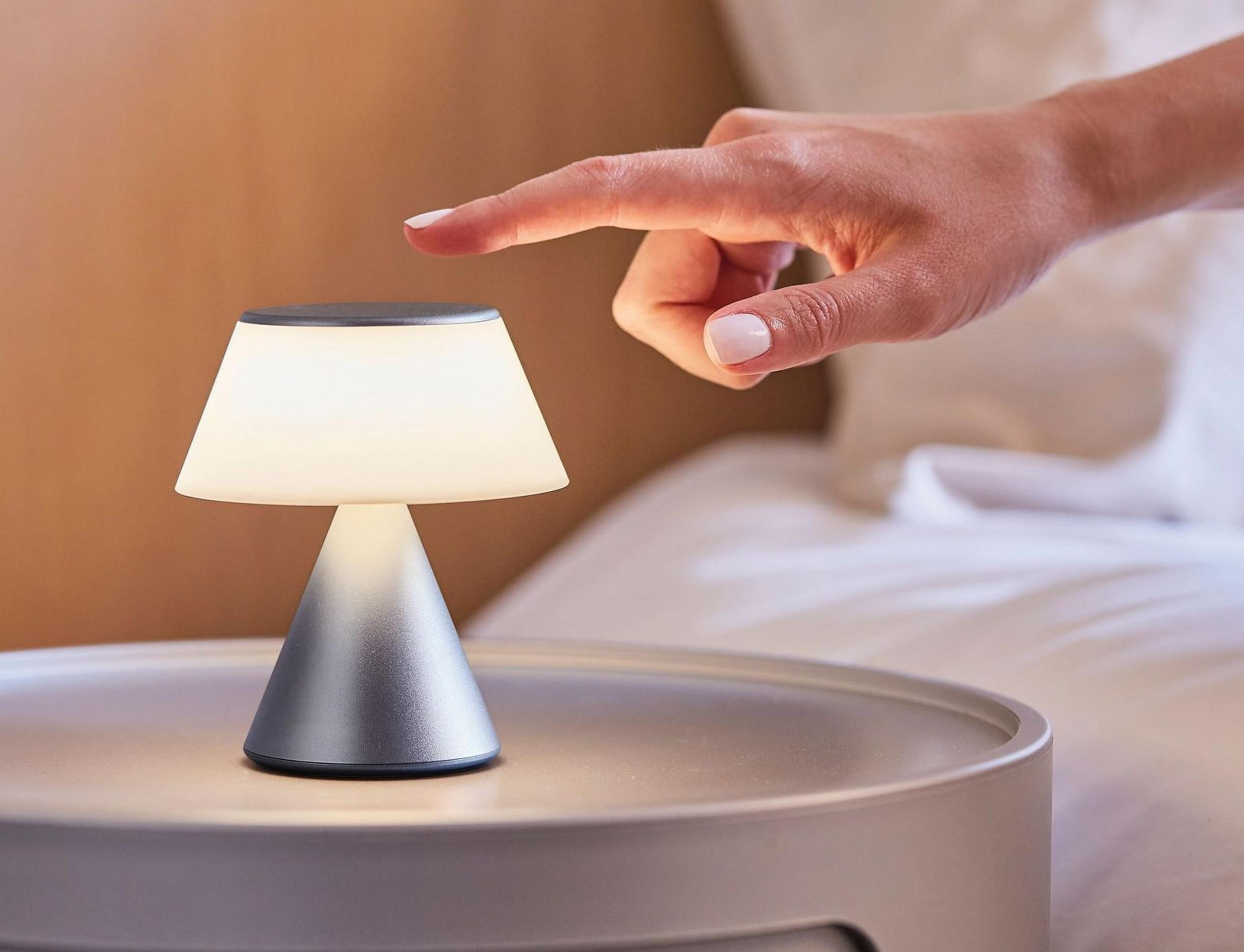 Una mano tocca una piccola lampada da comodino illuminata su un tavolo rotondo.