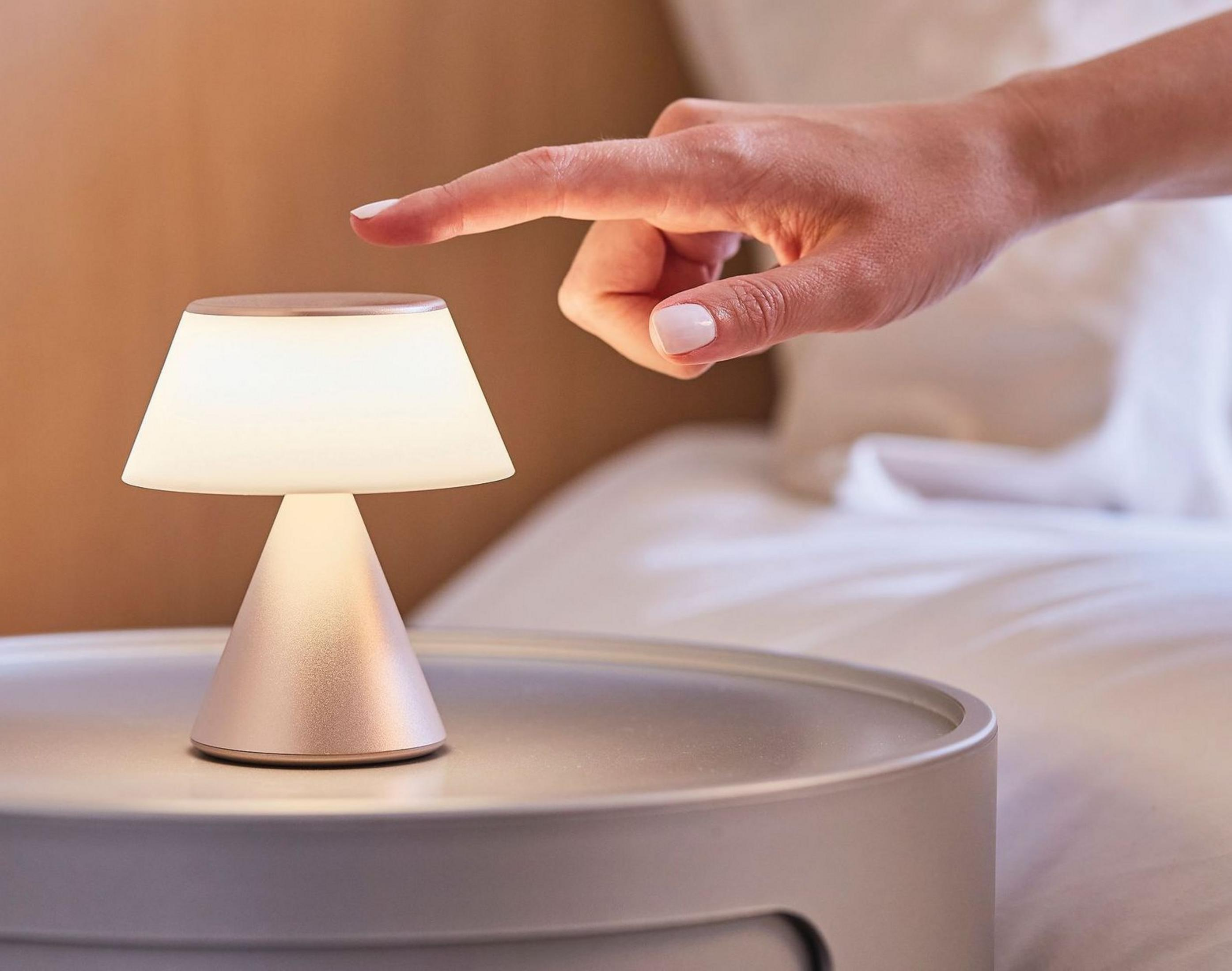Una mano tocca una piccola lampada da comodino accanto a un letto.