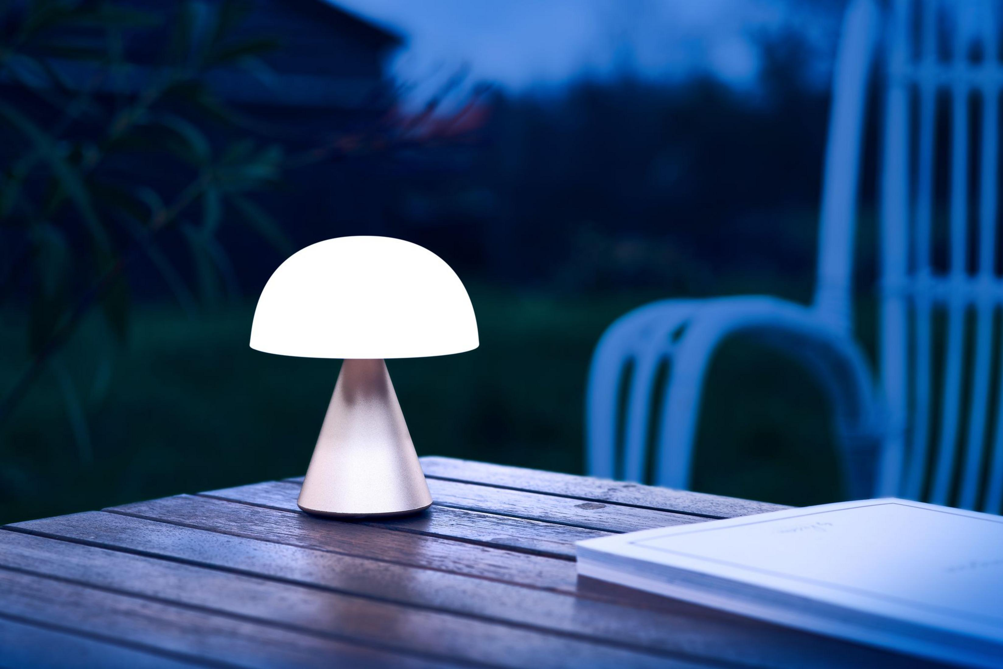 Une lampe champignon allumée sur une table en bois extérieure la nuit.