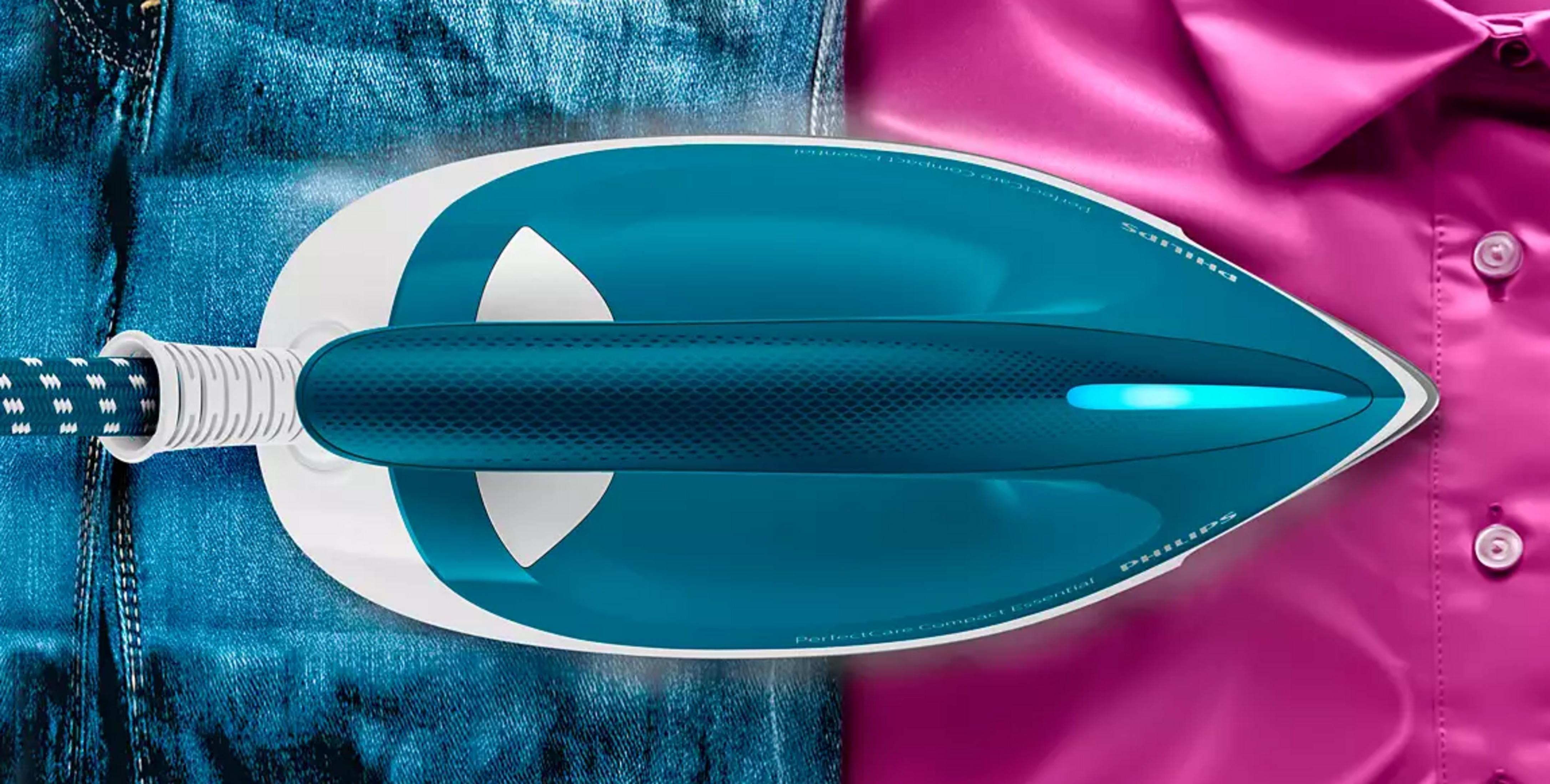Un fer à vapeur bleu repasse une chemise rose à côté d'un jean.