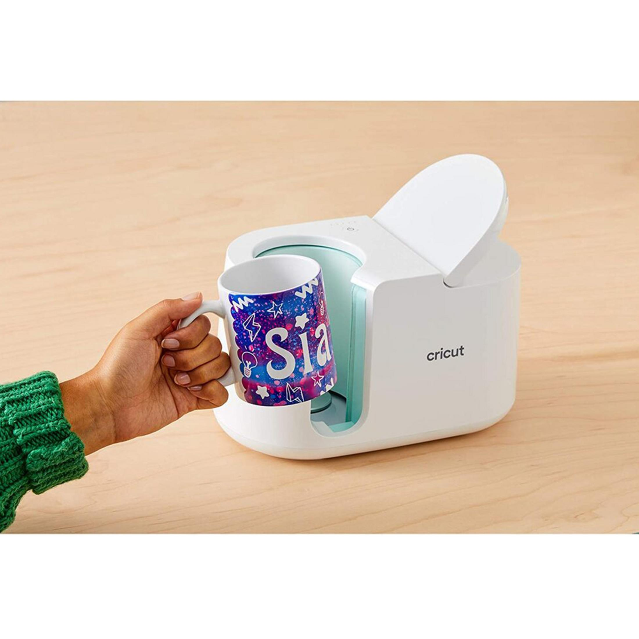 Una mano tiene una tazza con il nome 'Sia' davanti a una macchina Cricut bianca.
