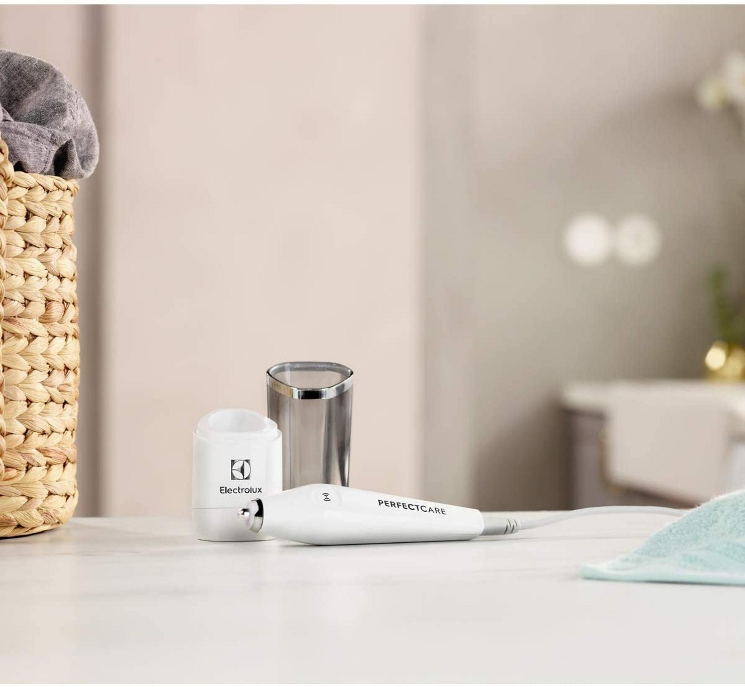 Białe urządzenie PerfectCare, szklanka i kosz na pranie na stole.