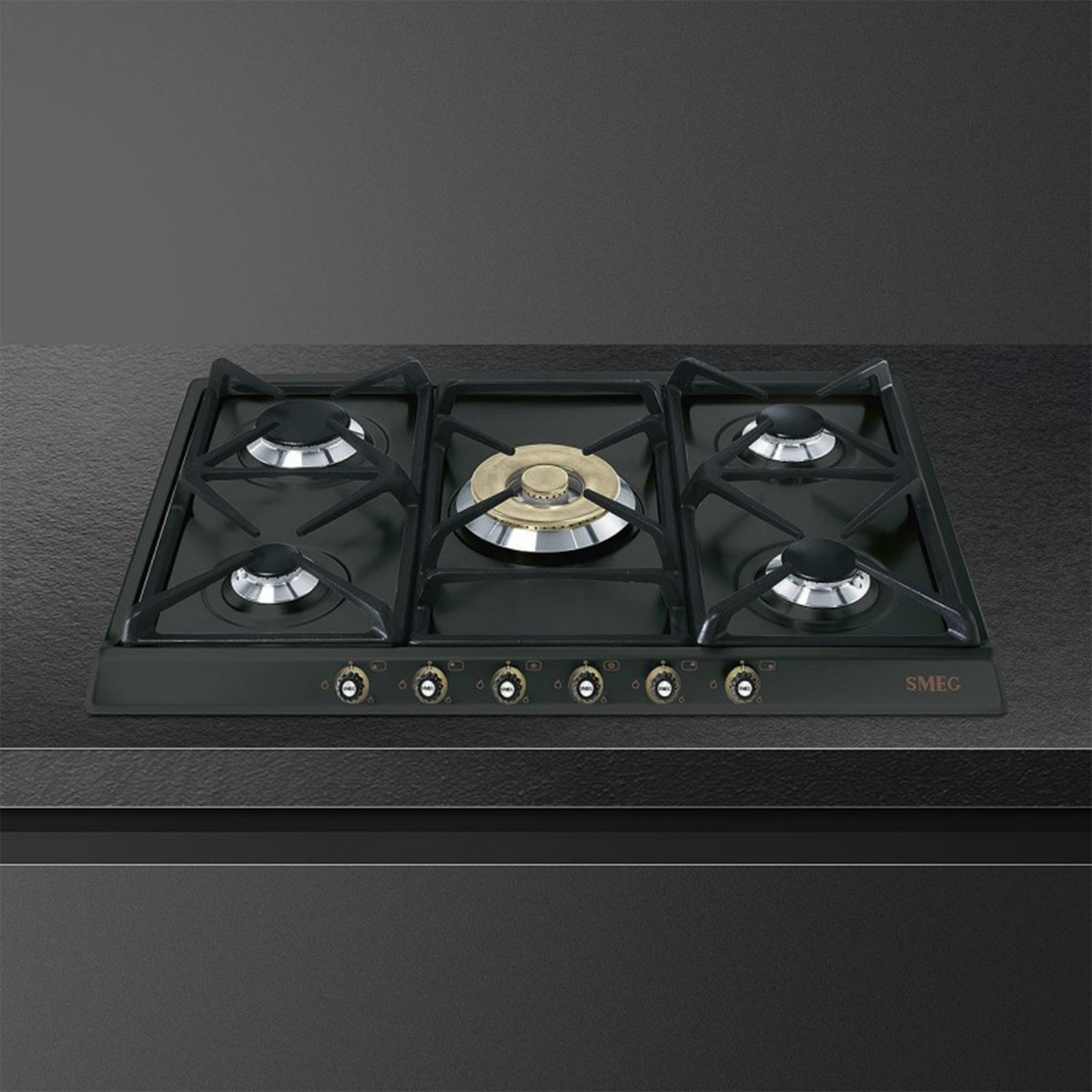 Placa de gas negra con cuatro quemadores y tapas plateadas, quemador dorado en el centro.