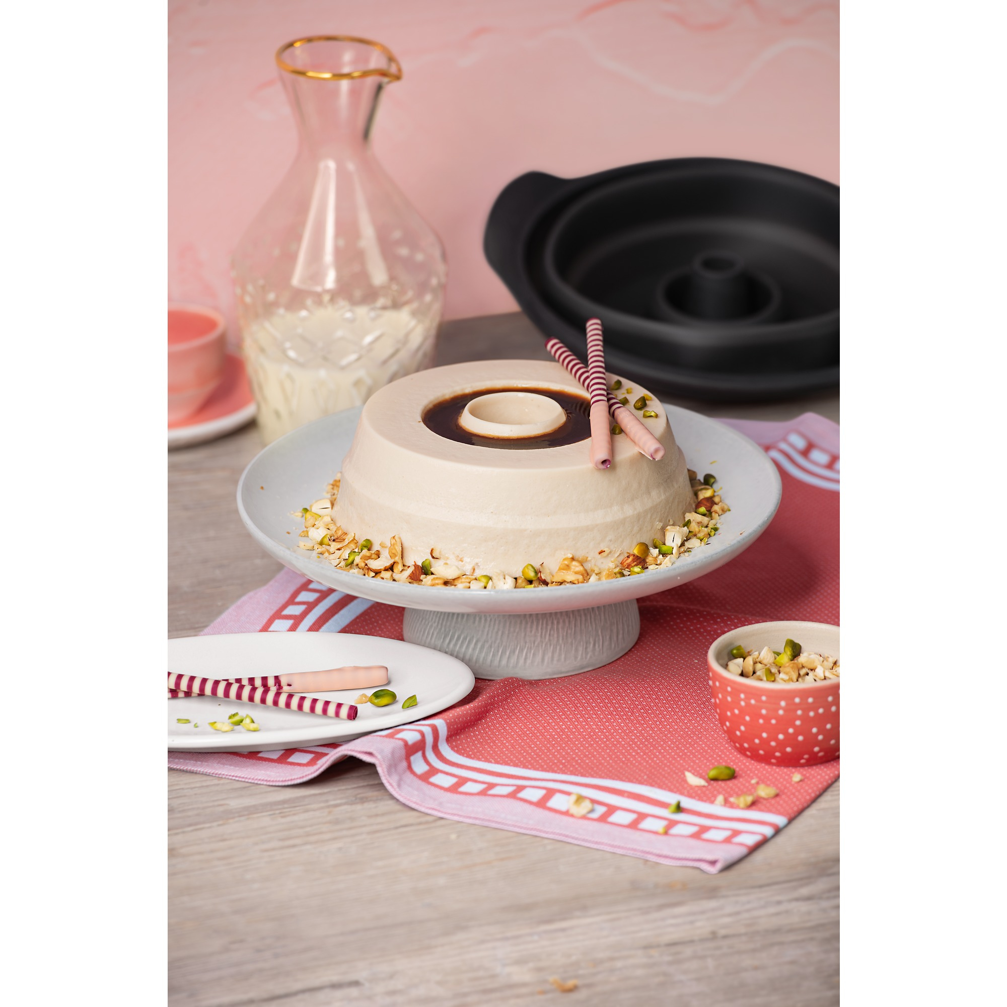 Ein heller Kuchen mit Schokoglasur, Nüssen und Gebäck auf einem Kuchenteller.