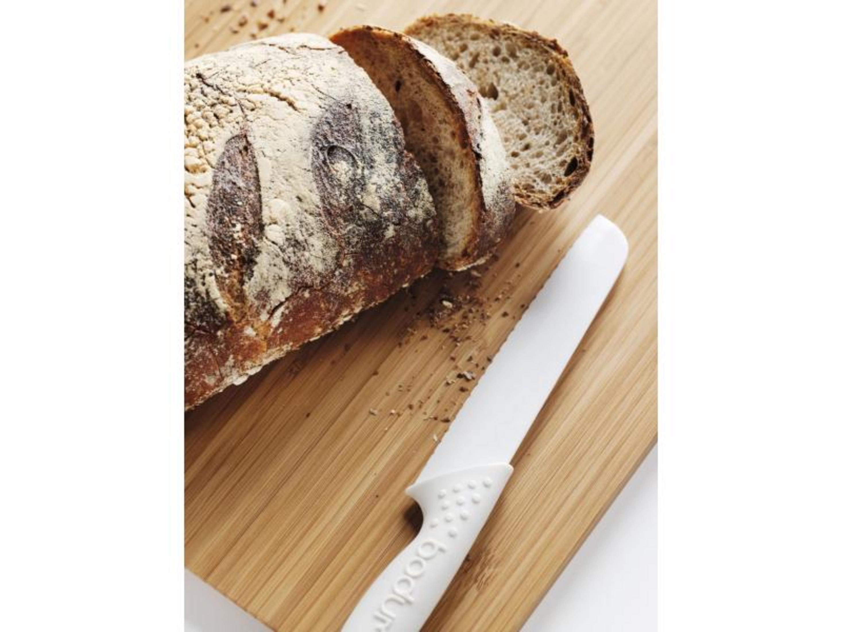 Ein angeschnittenes Brot liegt auf einem Holzbrett neben einem weißen Messer.