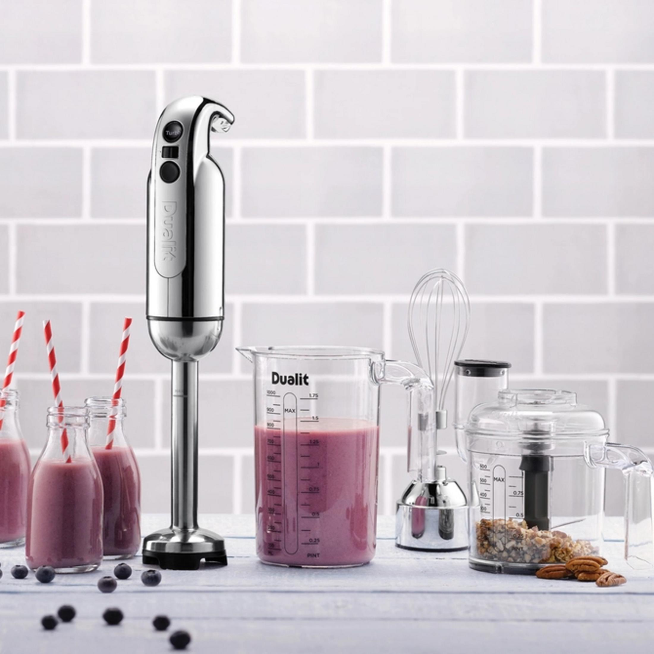 Ein silberner Stabmixer mit Zubehör, Becher mit Smoothie und Nüsse.