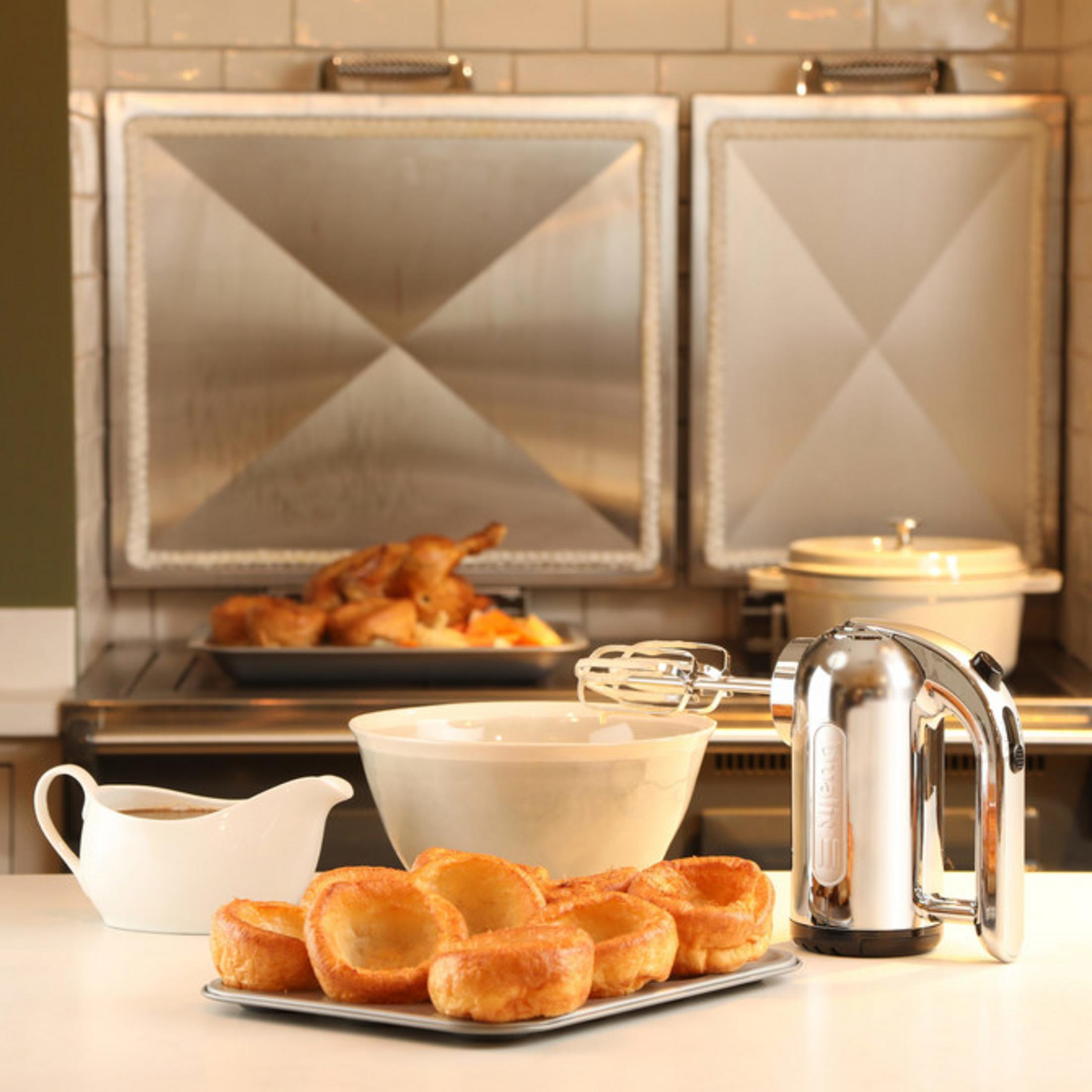 Un poulet rôti, des Yorkshire puddings, de la sauce et un batteur sont sur un comptoir.