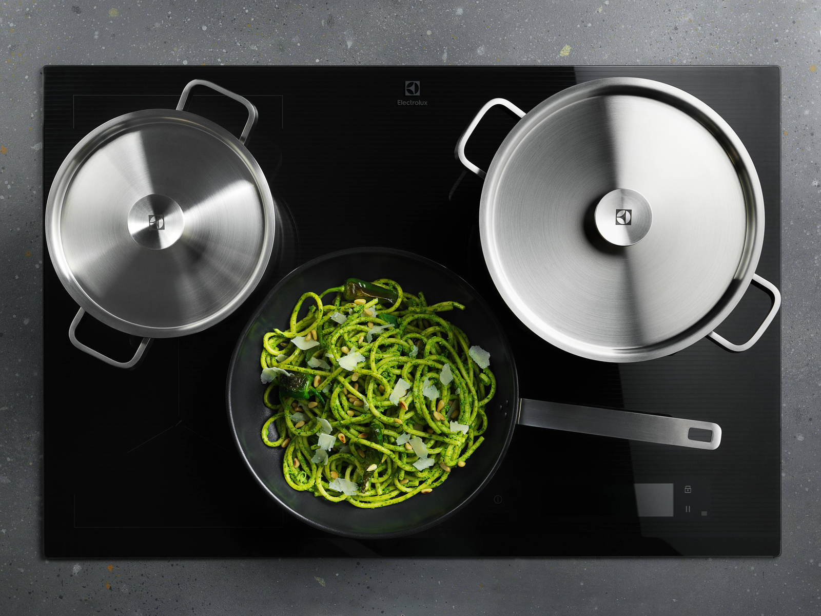 Una vitrocerámica con una olla, una sartén con pasta verde y otra olla.