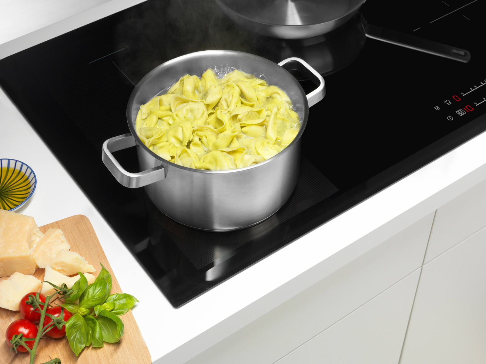 Tortellini hirviendo en una olla sobre una vitrocerámica con ingredientes al lado.